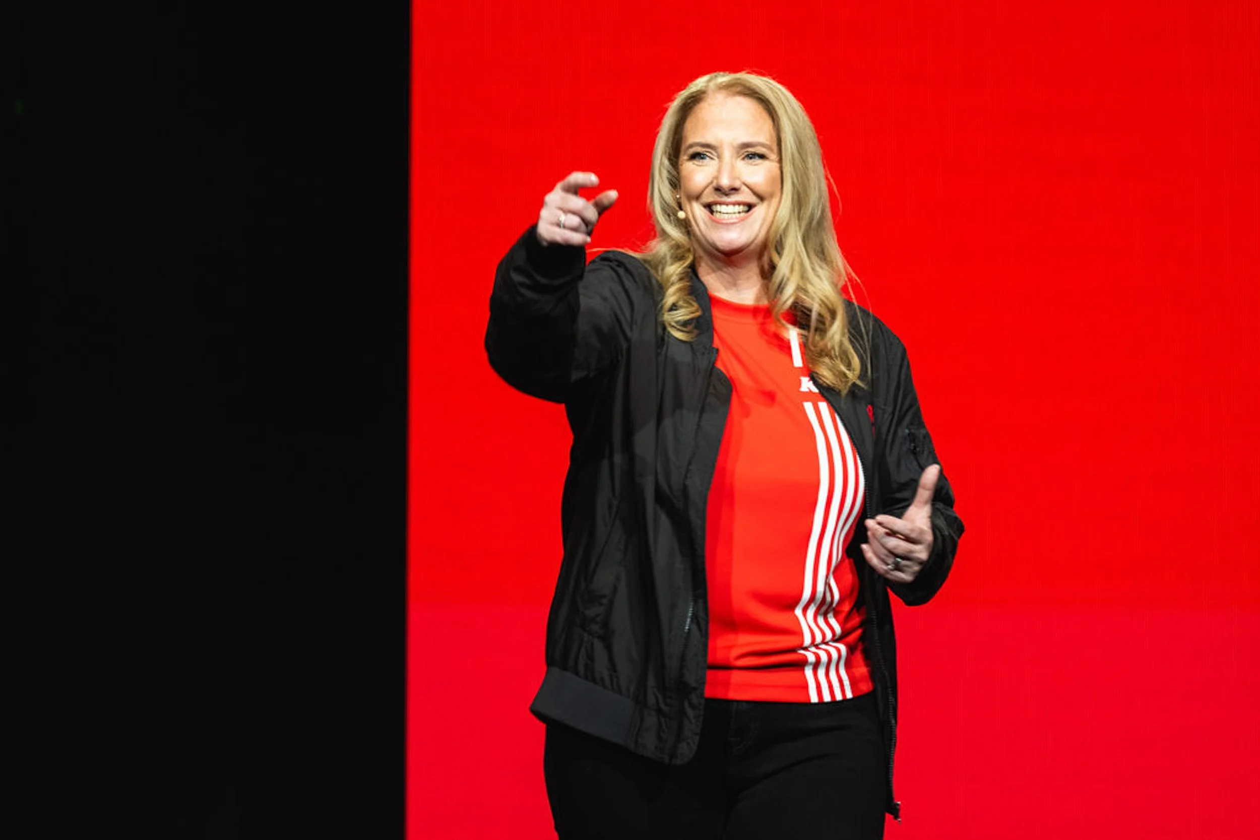 Speaker smiling and gesturing on stage against a red backdrop.