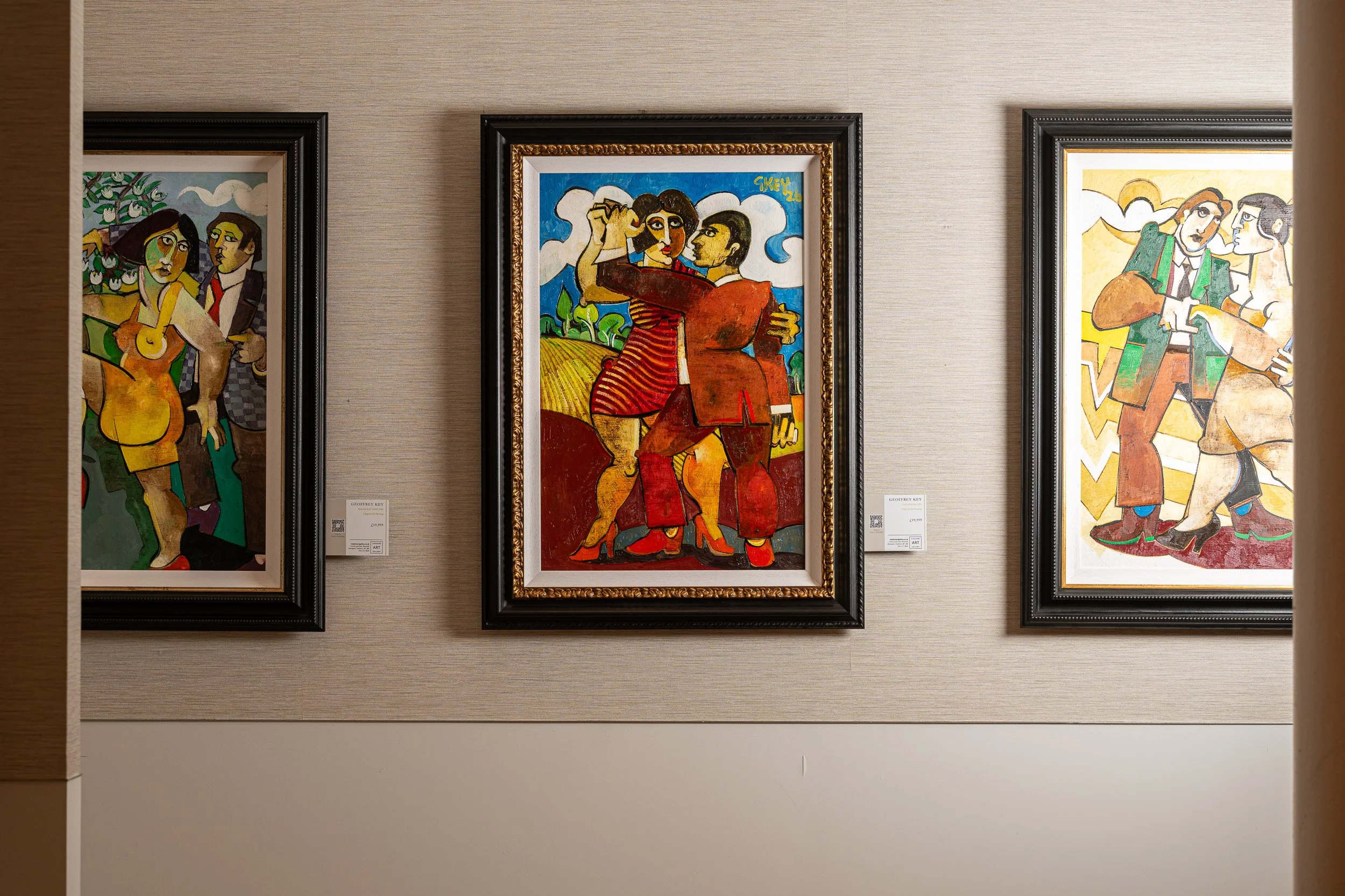 Three colourful figurative paintings displayed together on a pale wall.