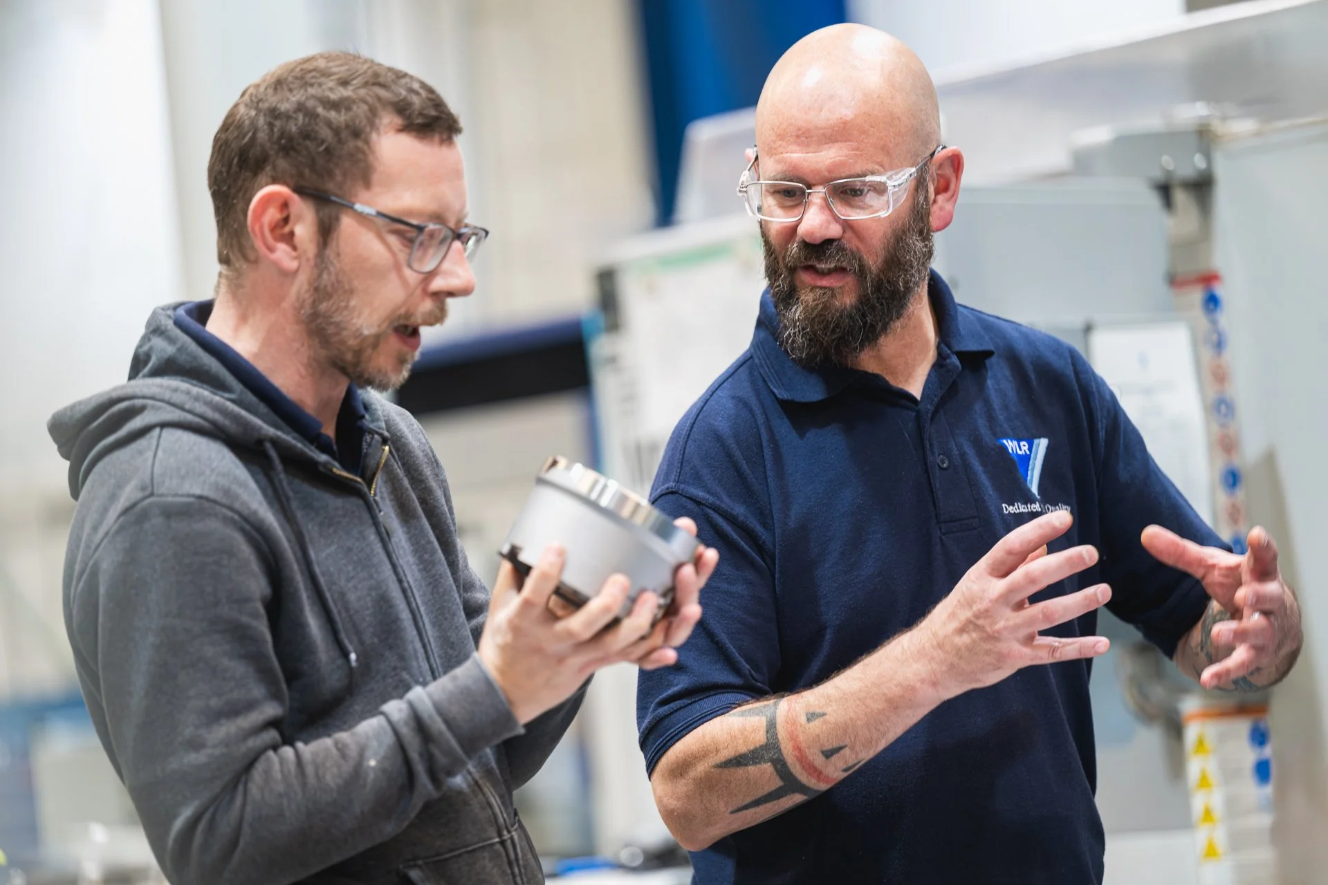 Two colleagues discussing a metal component on the factory floor.