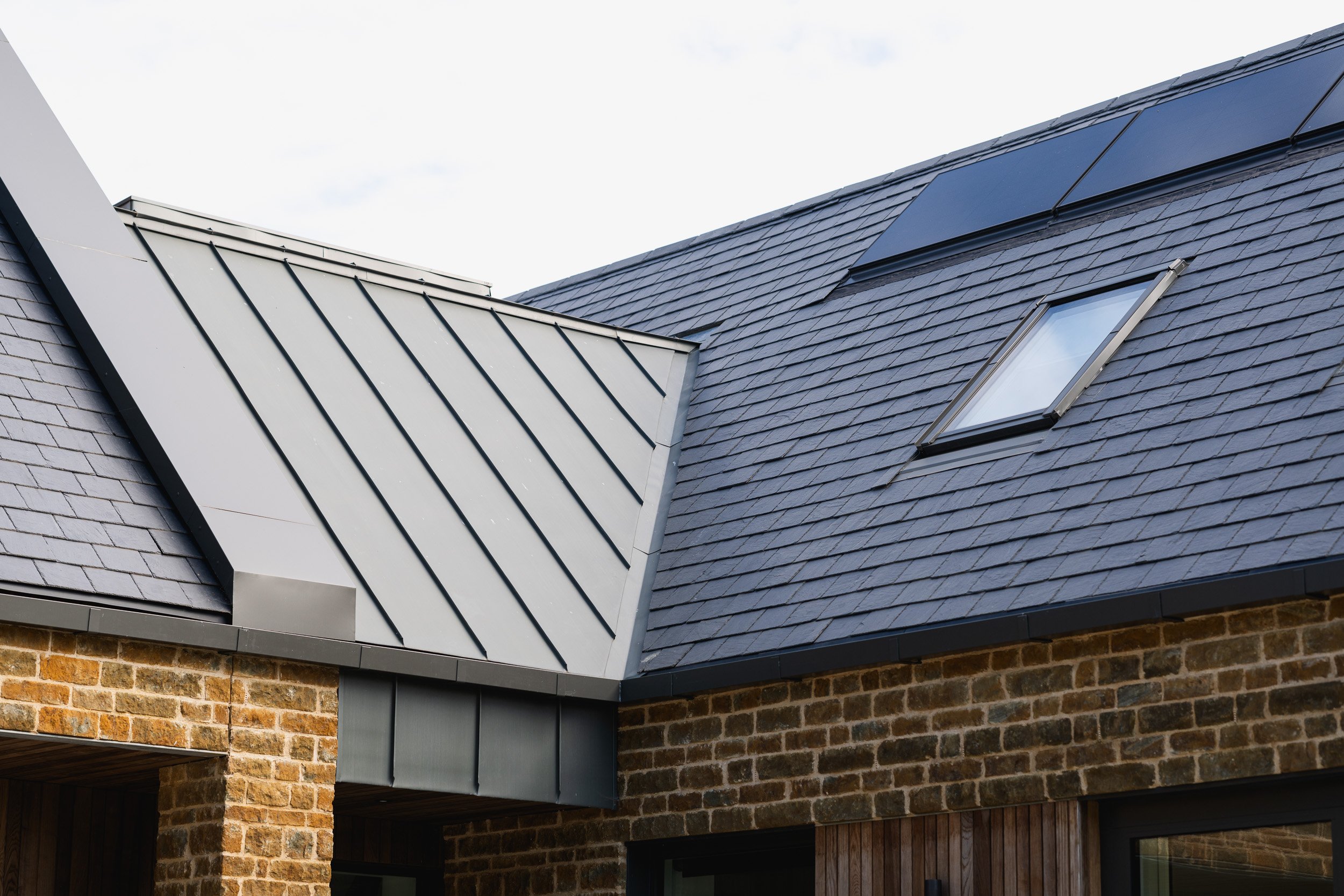 Close view of a standing-seam roof meeting a slate roof above stone walls.