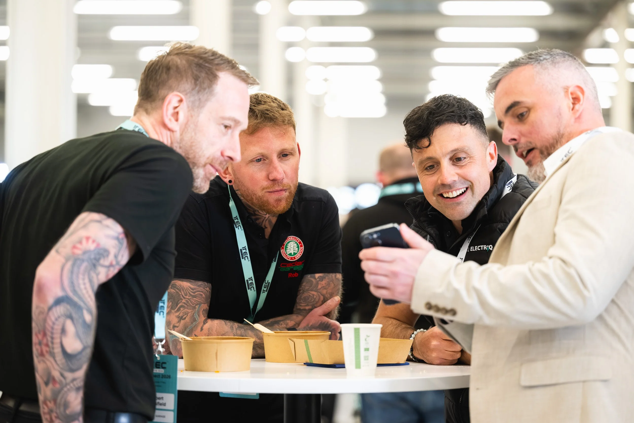 Four delegates looking at a phone around a table at the 1TEC conference.