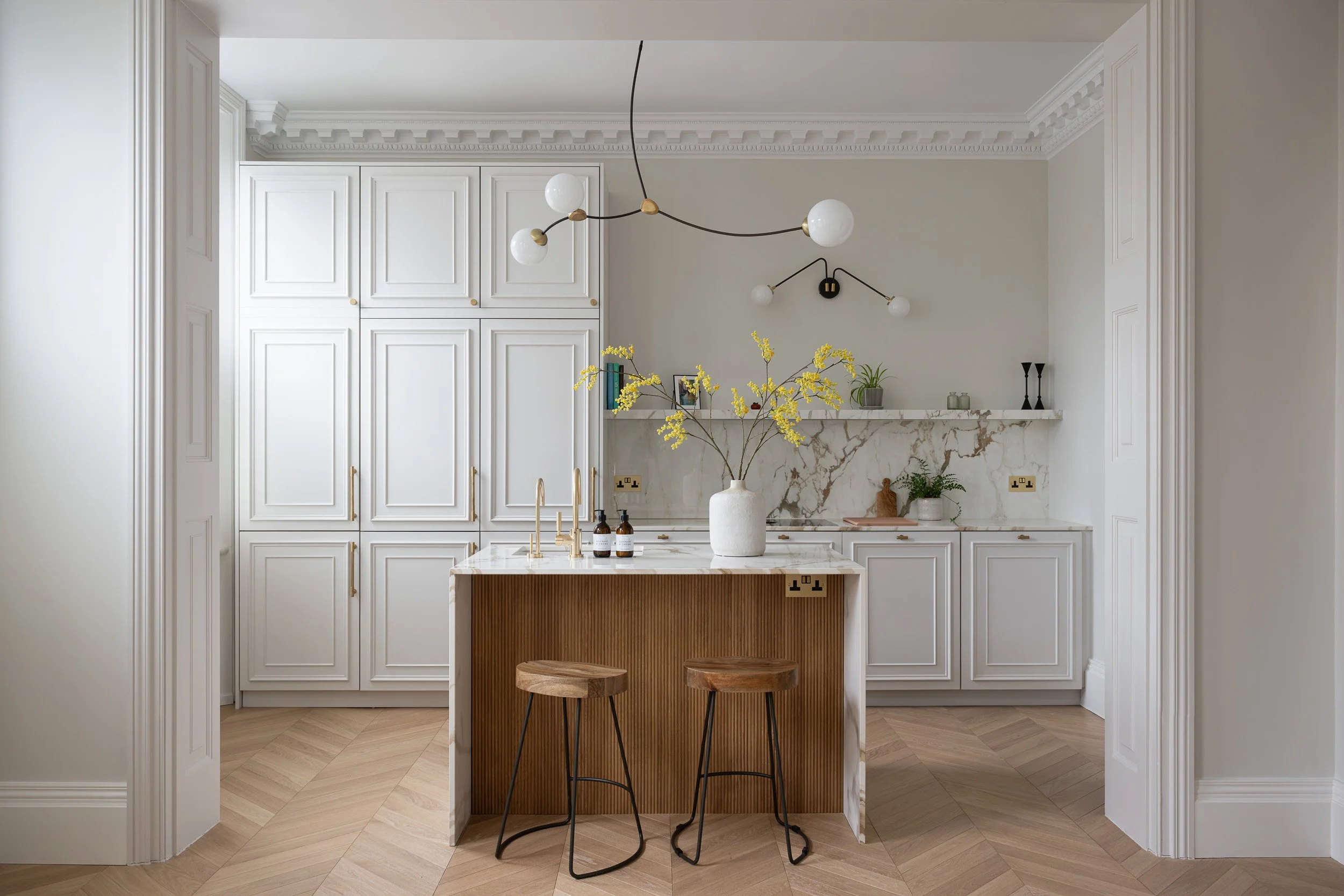 White panelled kitchen with a central island and timber stools