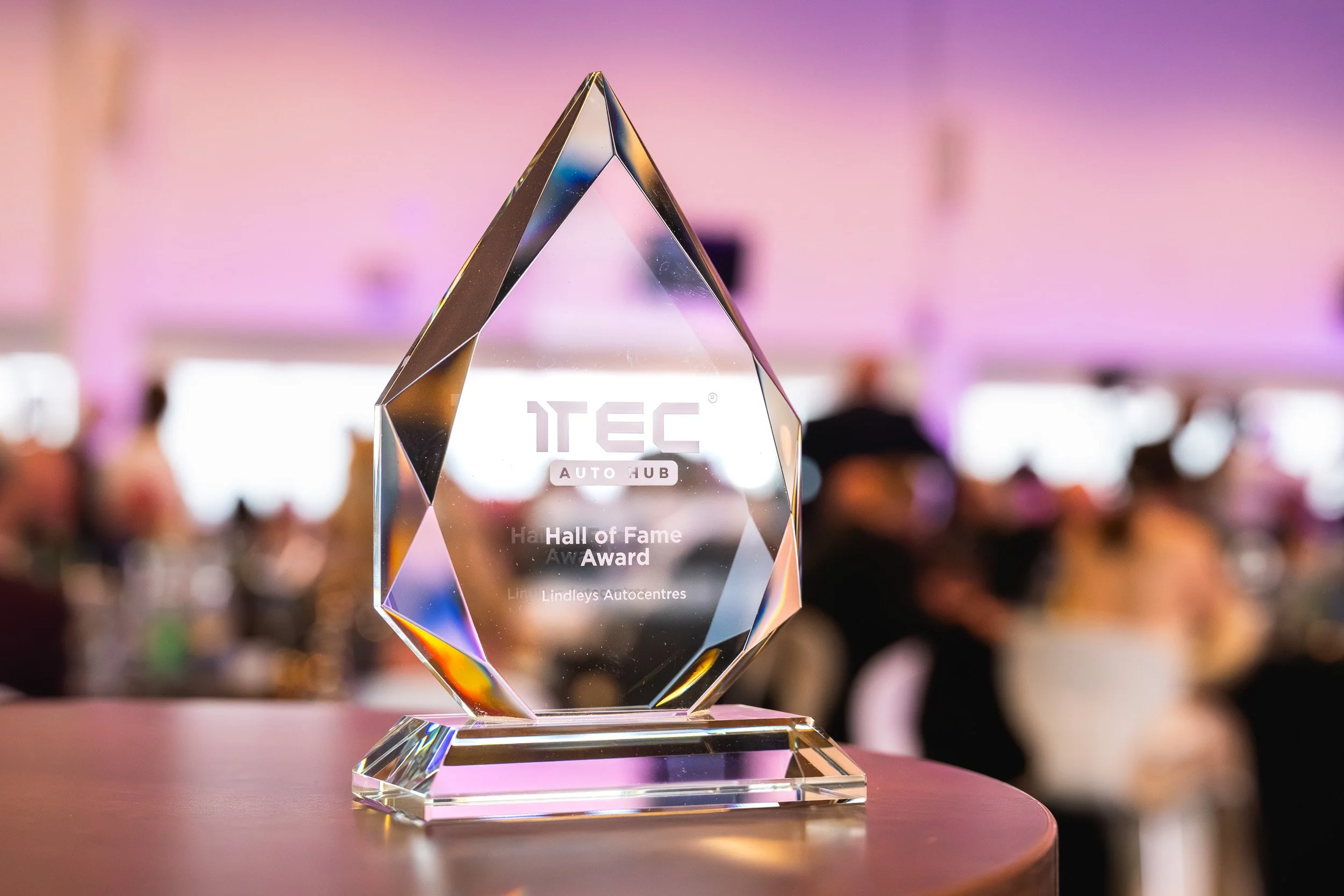 A glass 1TEC trophy on a table, with dinner guests blurred in the background.