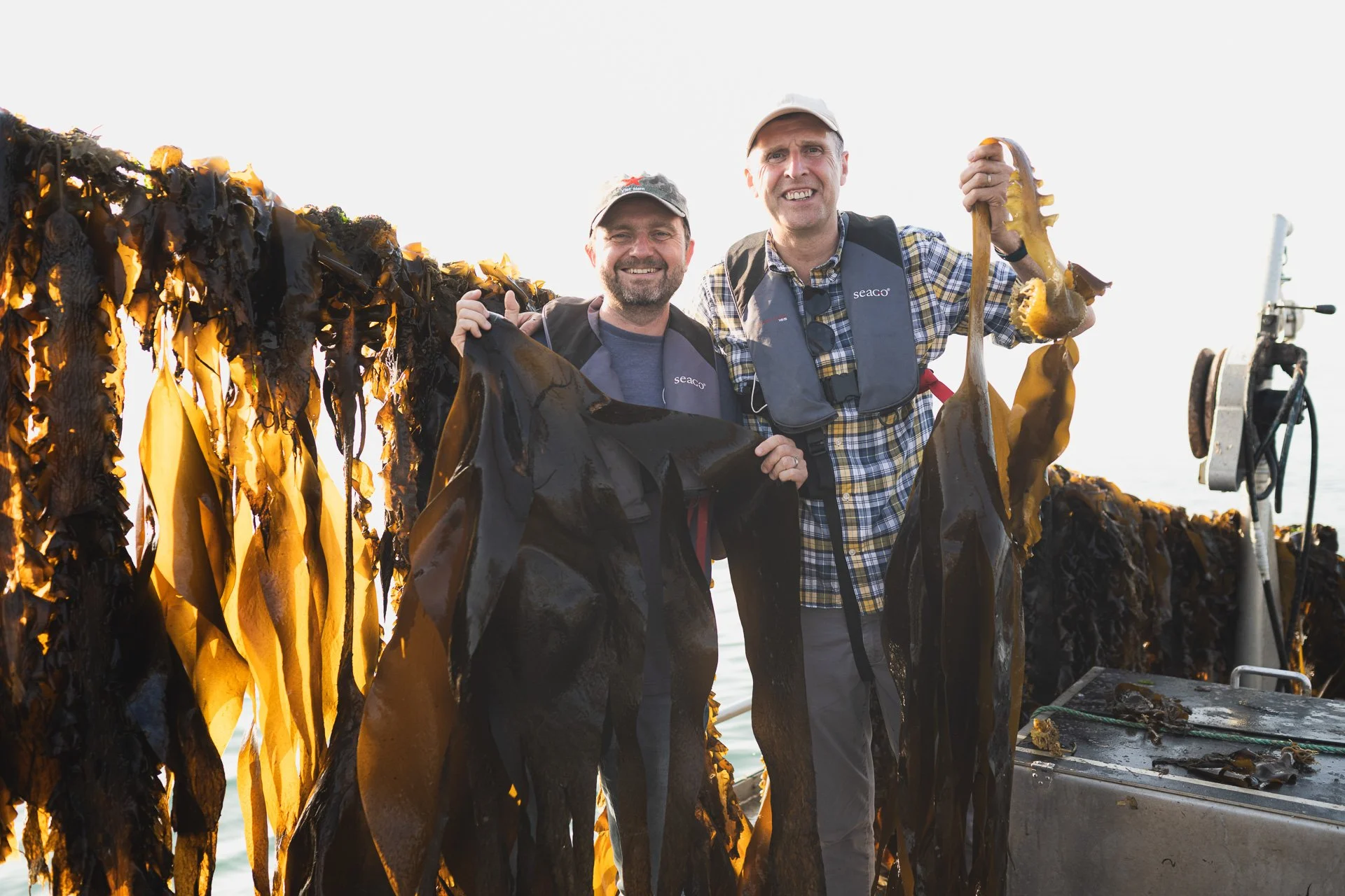 Two members of the Câr-y-Môr team holding harvested seaweed beside the boat.