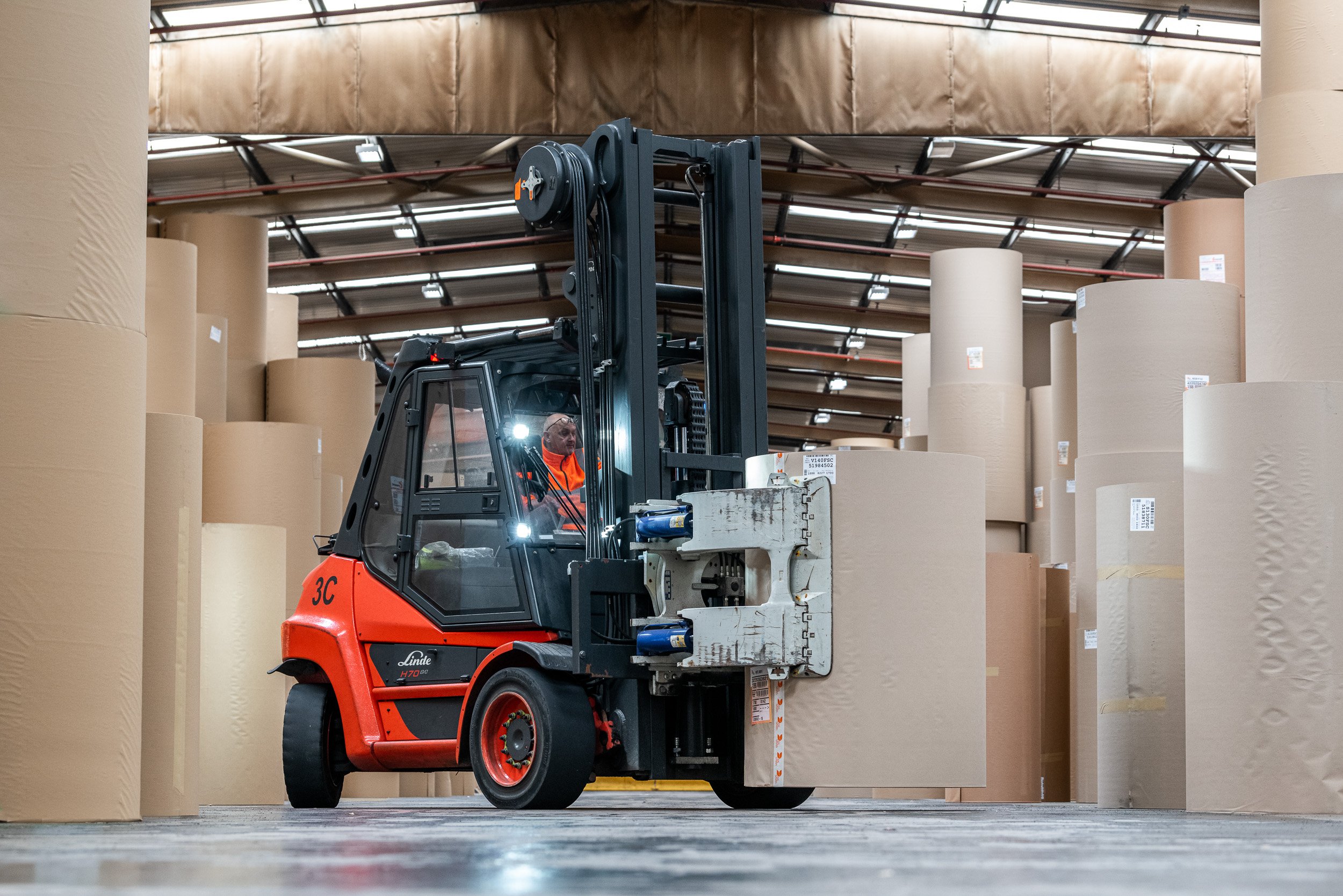 Forklift moving among large rolls of cardboard in a warehouse.