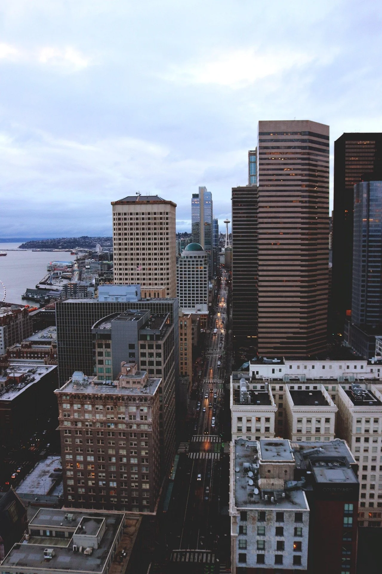 A cityscape of downtown Seattle, Washington, with tall modern buildings, streets, and the Space Needle visible in the distance, under a cloudy sky.