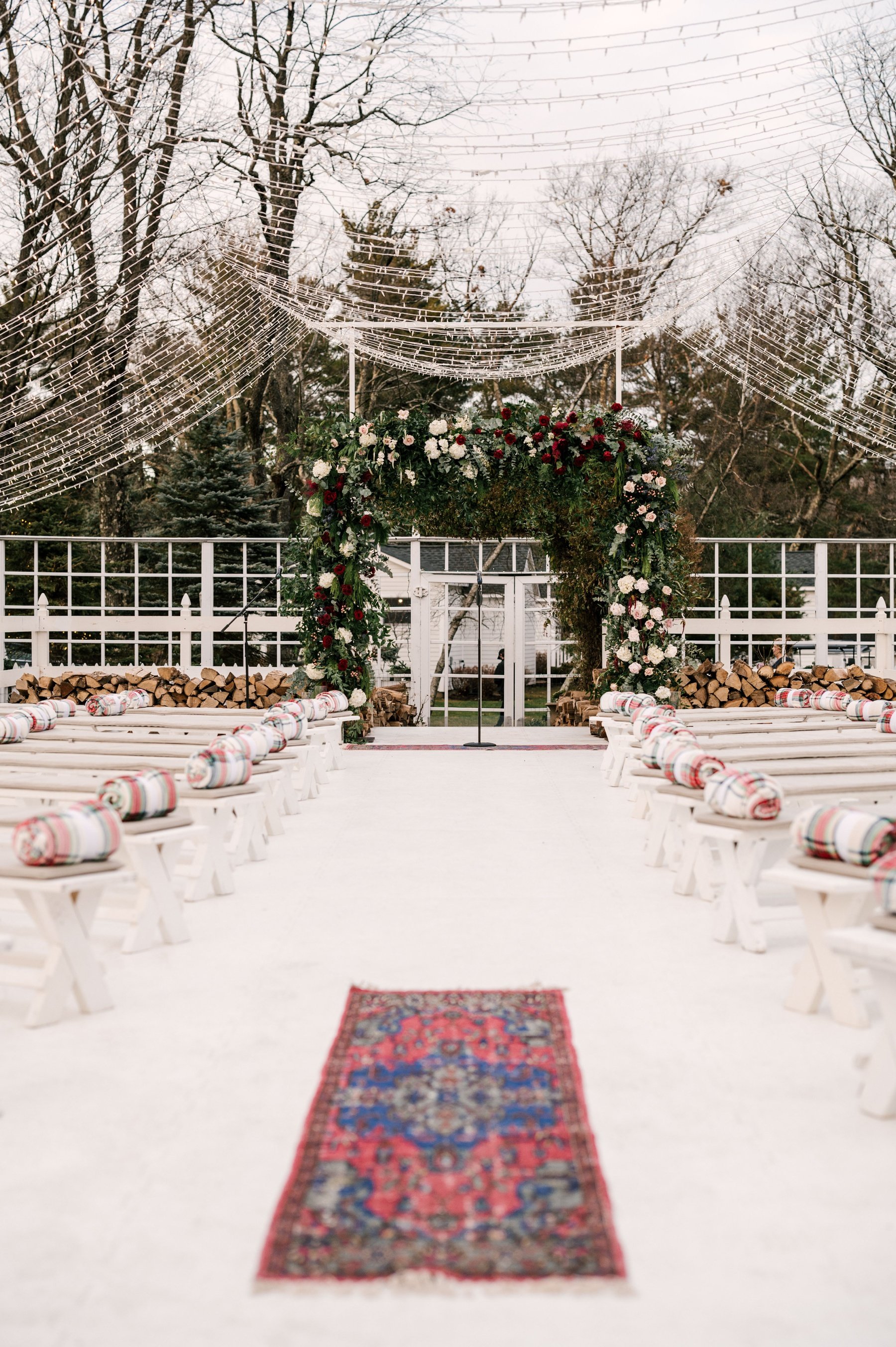 Winter wedding ceremony with vintage rugs, plaid blankets, and bistro lights