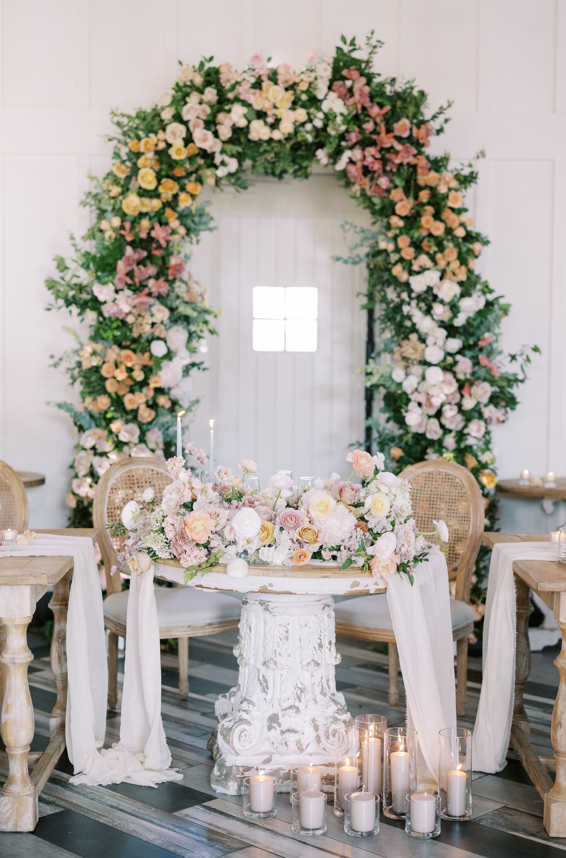 French Country sweetheart table with cane back chairs, pastel flowers, and a gauze runner