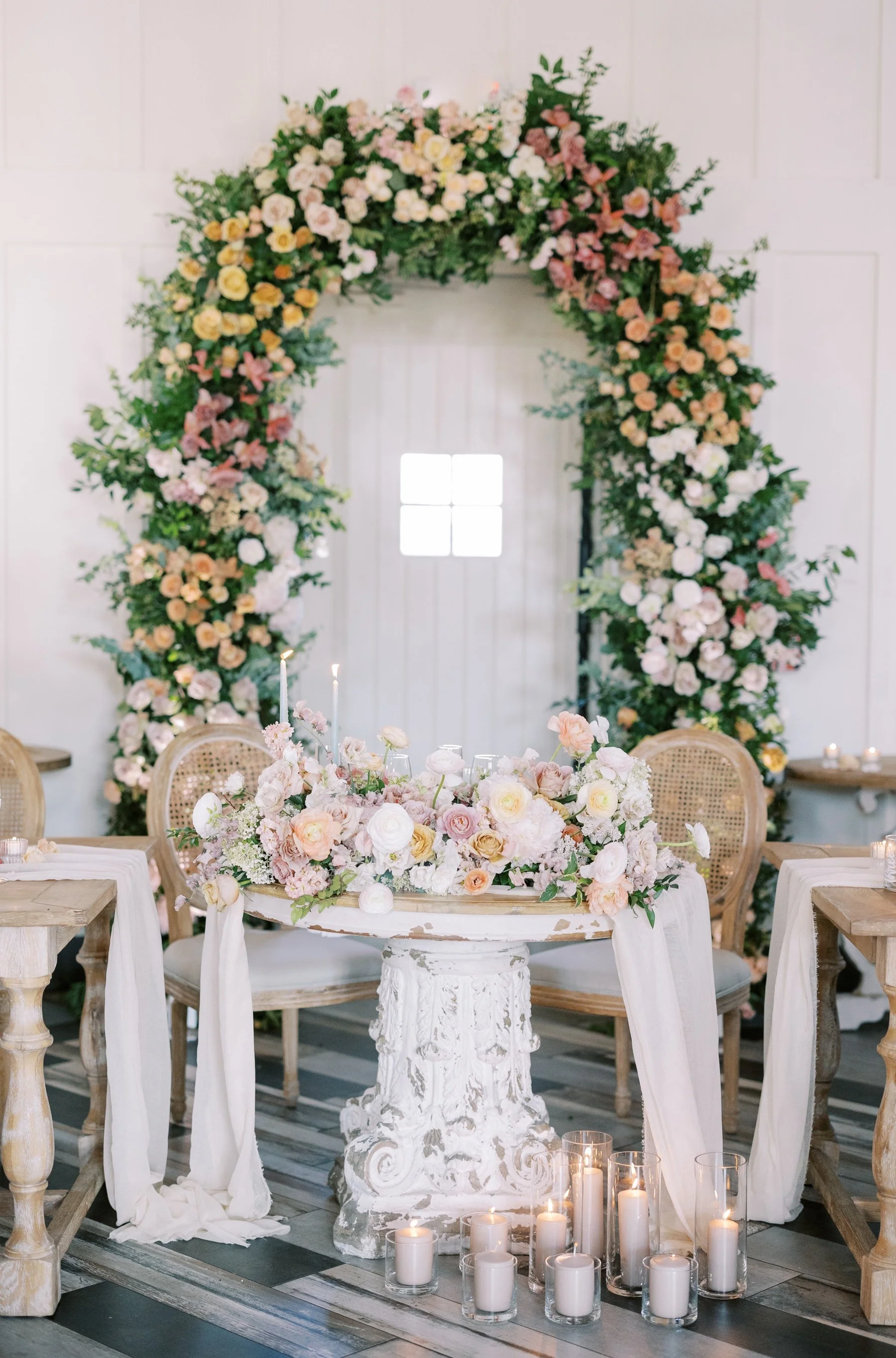 French Country sweetheart table with cane back chairs, pastel flowers, and a gauze runner