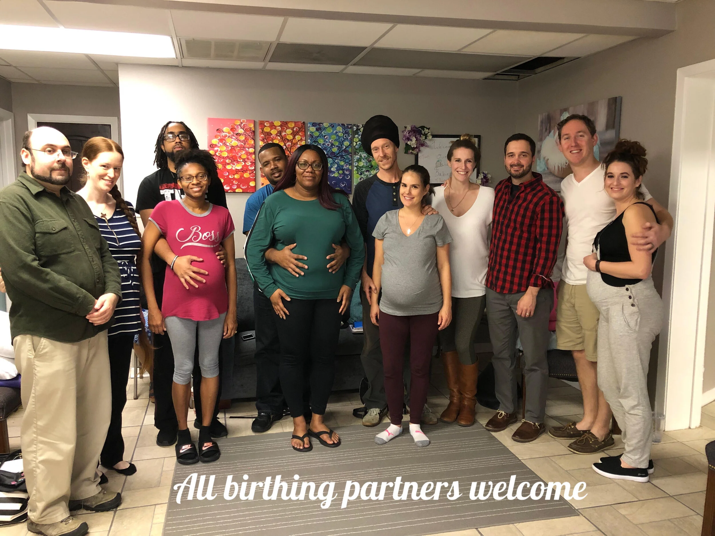 The Bradley Method group course attendees, including pregnant women, smiling inside a room with colorful wall art, some embracing or holding their bellies, with a text overlay saying "All birthing partners welcome."