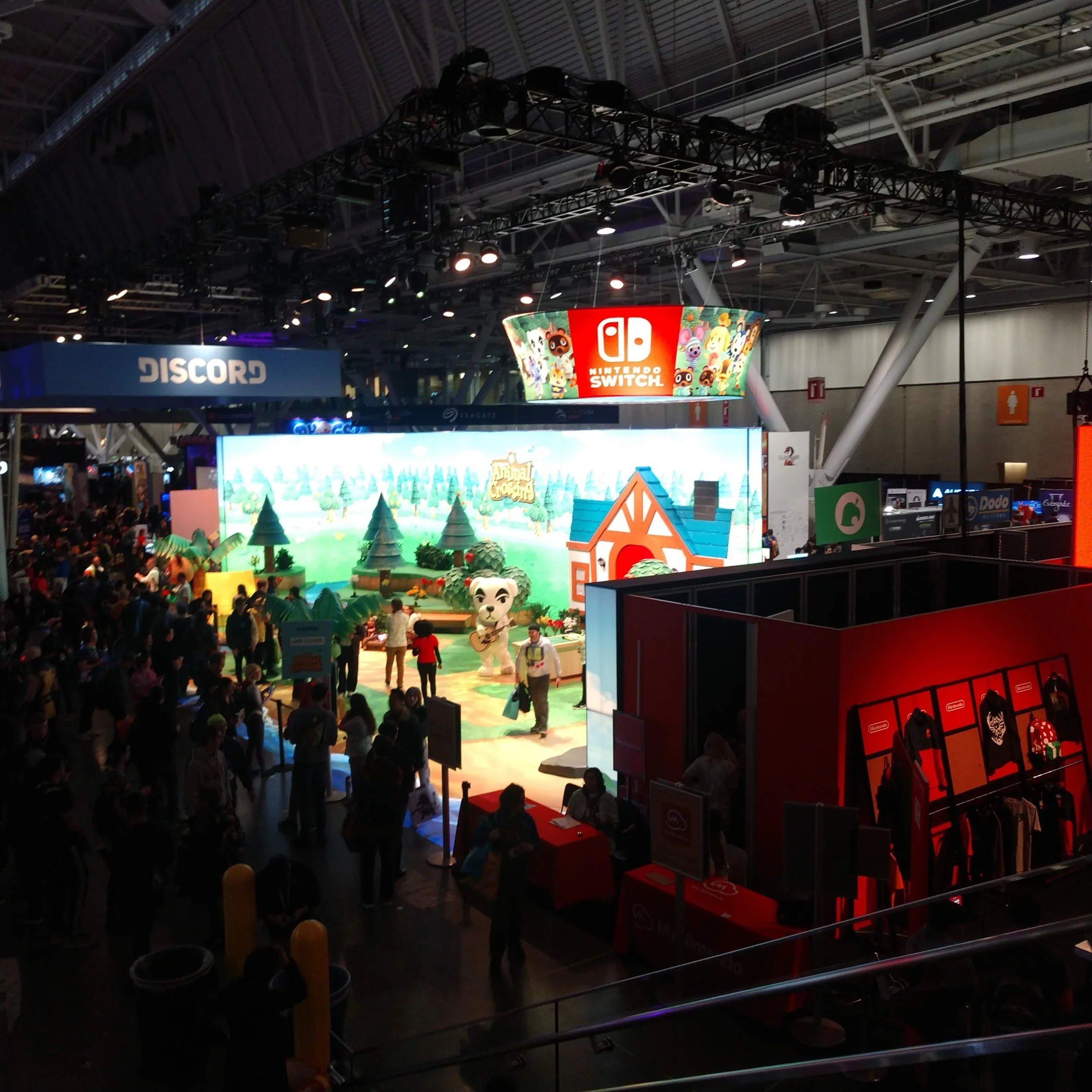 Indoor gaming convention with crowded attendees, displays for Nintendo Switch and Animal Crossing, and booths such as Discord.