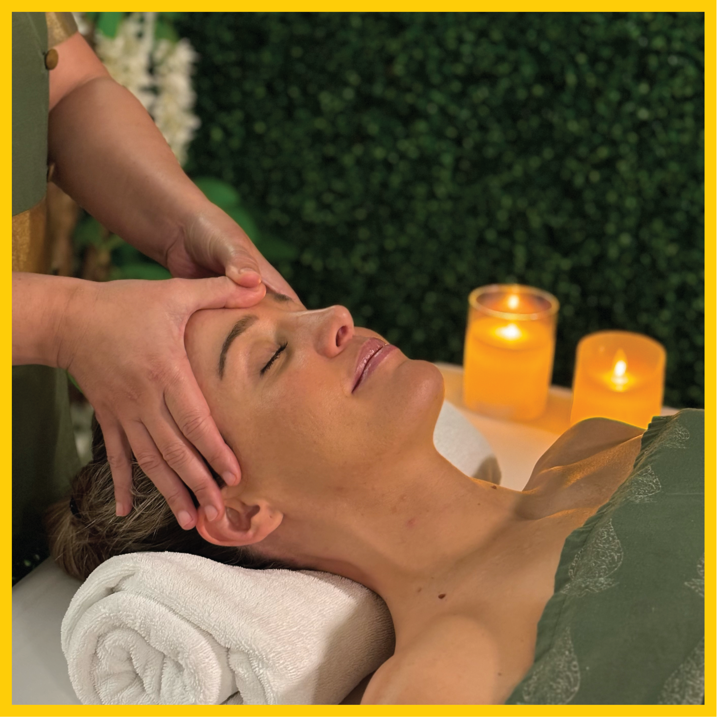 A woman receiving a relaxing facial massage at a spa, lying on a towel with candles in the background