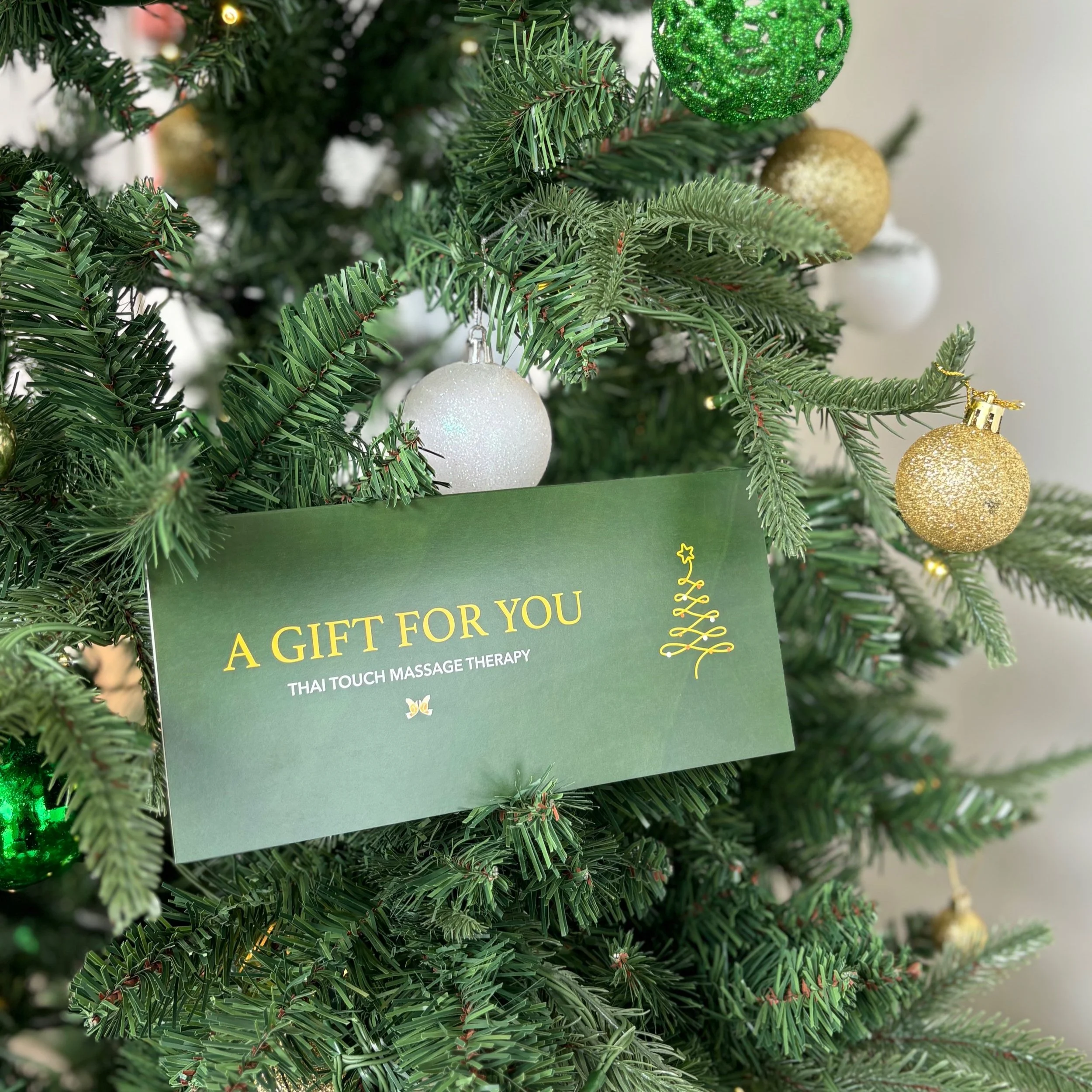Decorated Christmas tree with gold, white, and green ornaments and a green card reading 'A Gift For You, Thai Touch Massage Therapy'.