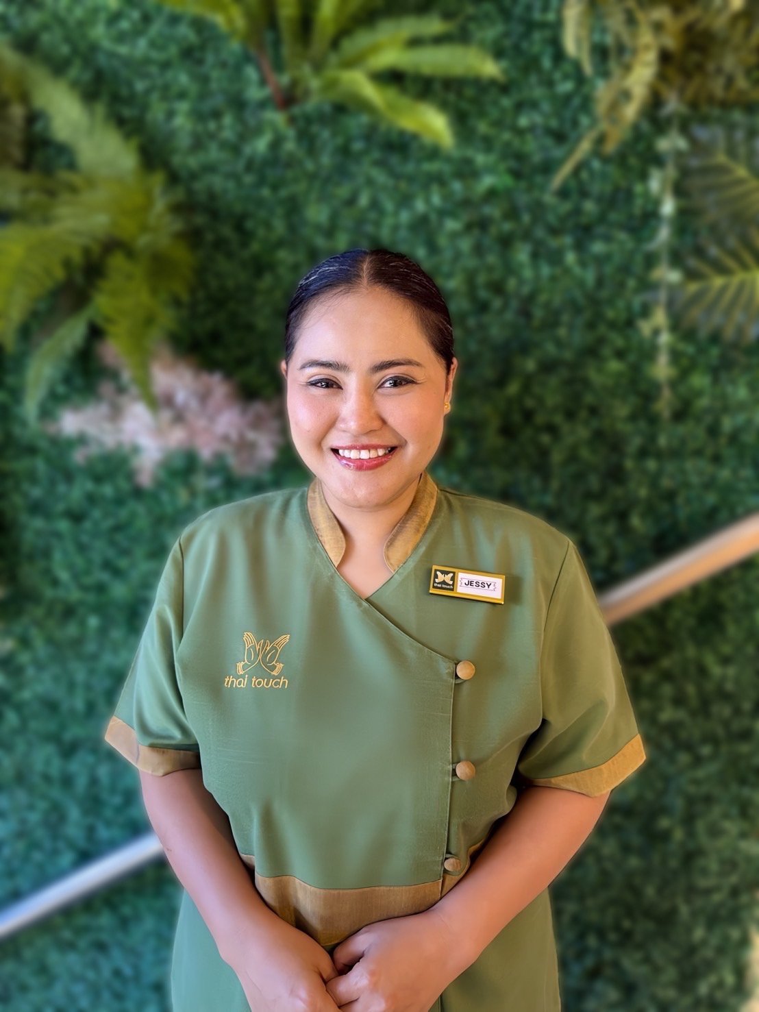 Thai Touch's Jessy, standing in front of a leafy green wall background.