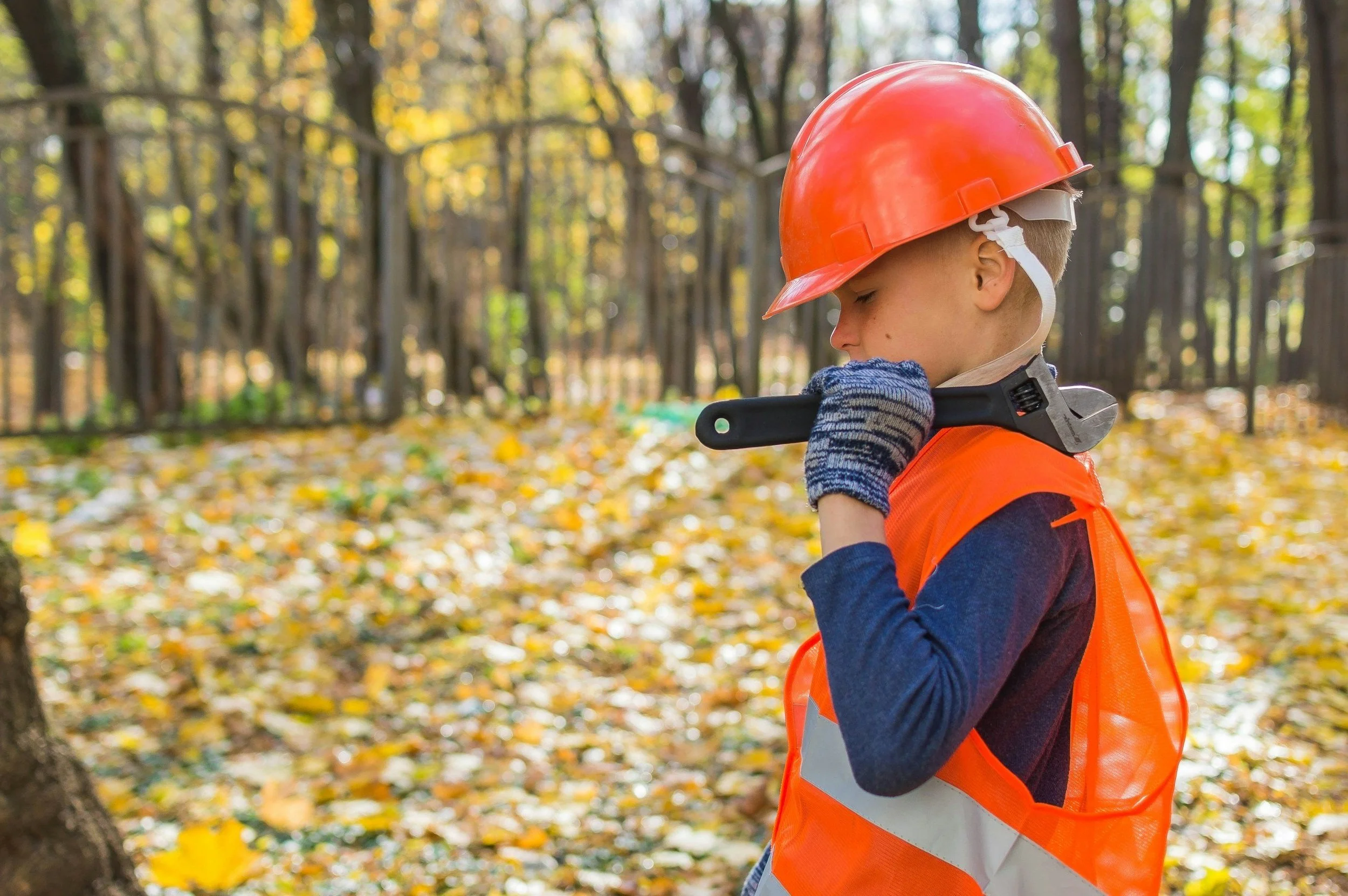 Child in safety gear holding a wrench in a forest setting.