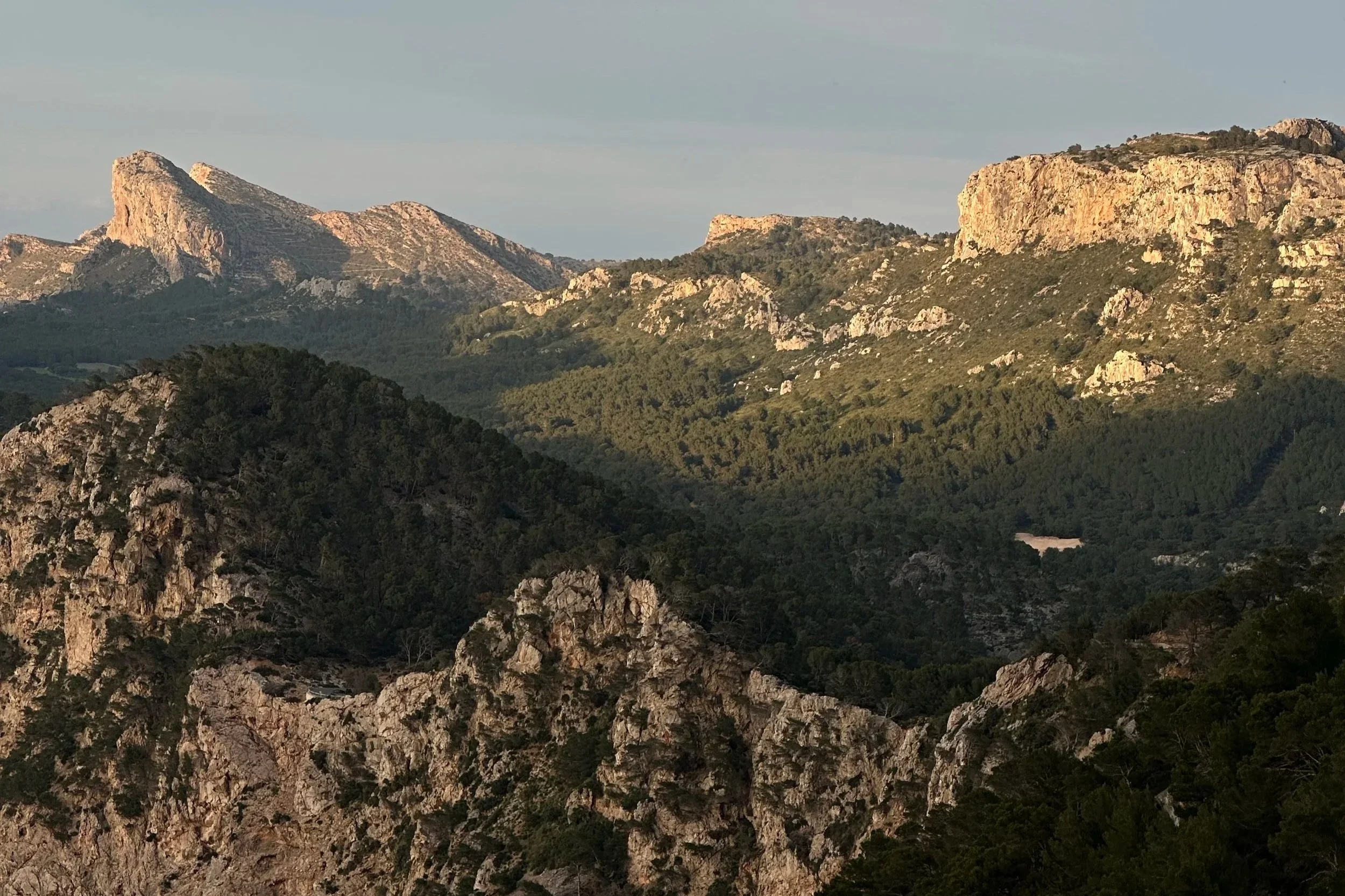 Scenic view of rugged mountains with rocky peaks and green forested slopes under a partly cloudy sky.