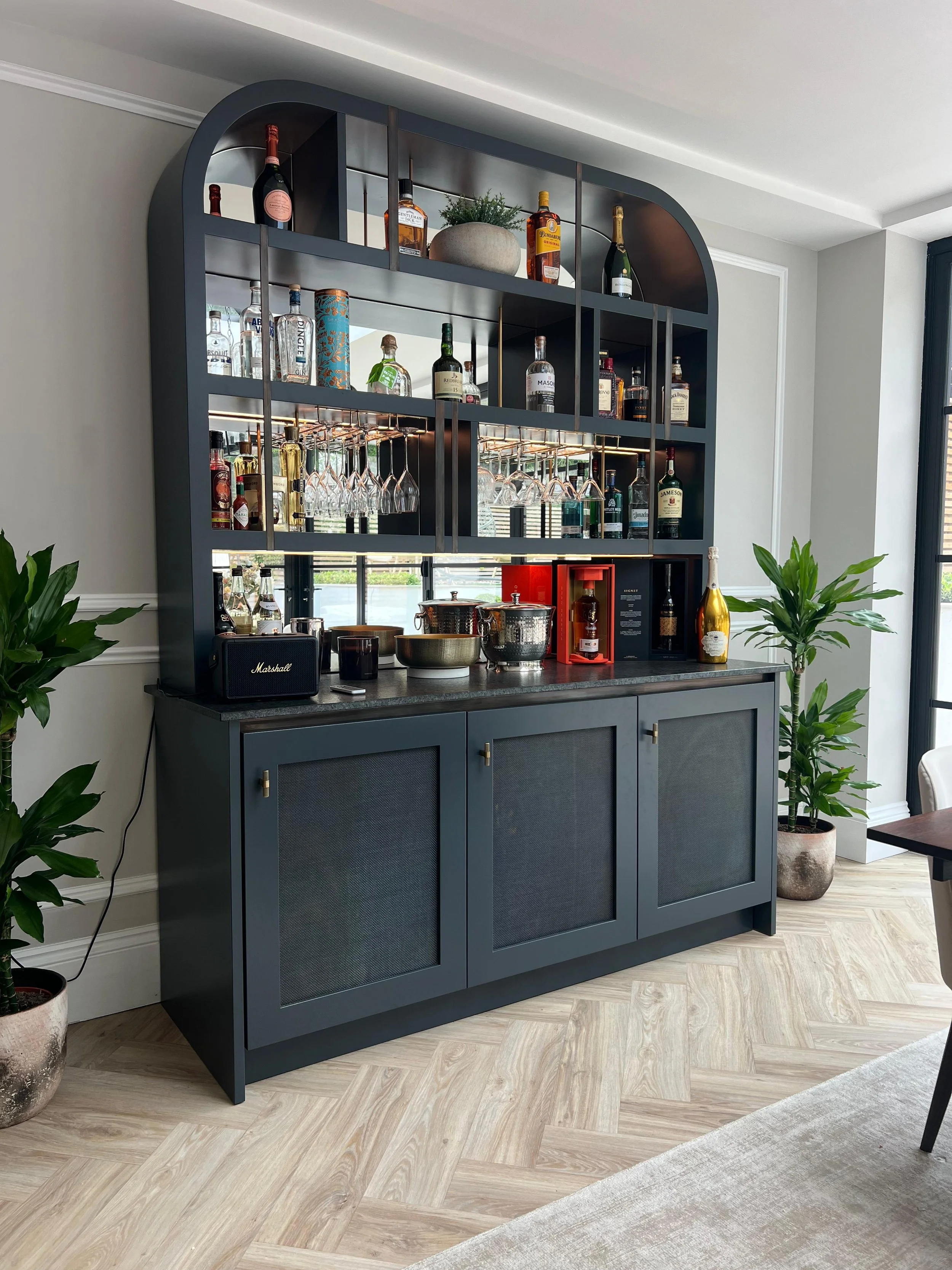 Private bar unit in London. Leathered black quartz worktop, brass mesh doors, copper strip detailing, mirror backed.