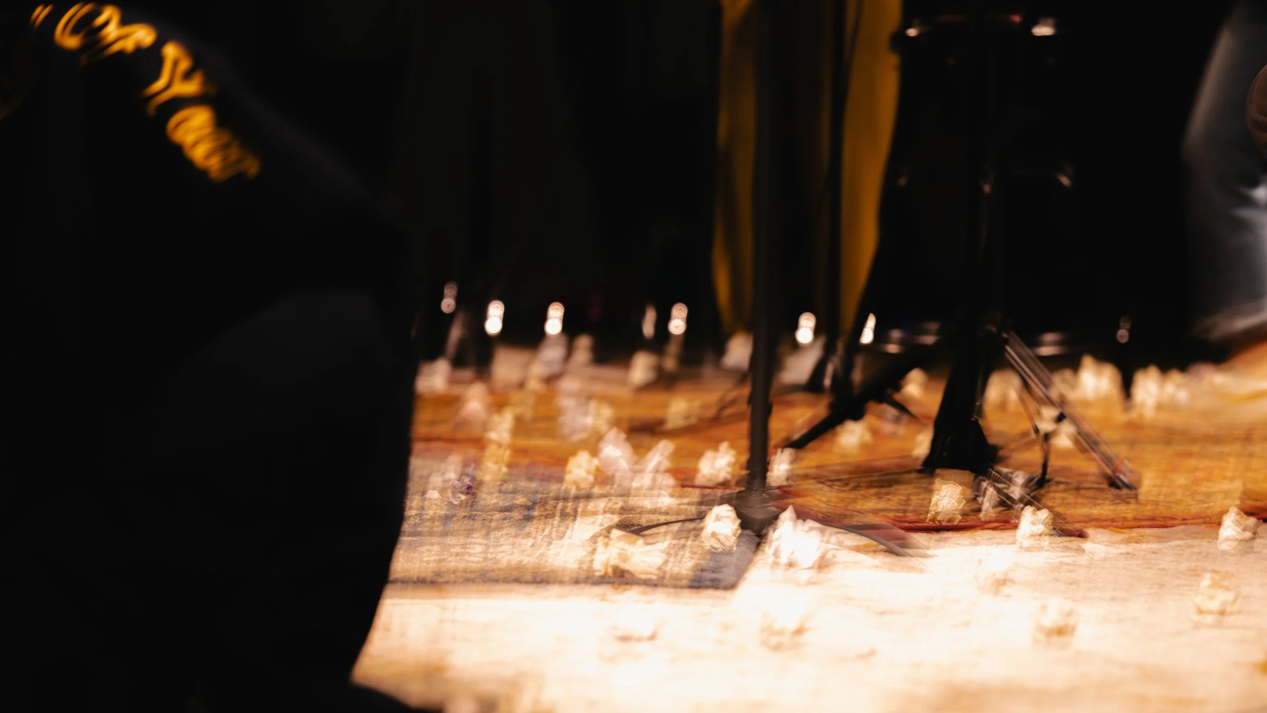 Close-up of musical stands and scattered popcorn on a stage with a wooden floor, part of a rug, and dark background.