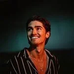 Smiling man with dark hair, wearing a black and white striped shirt