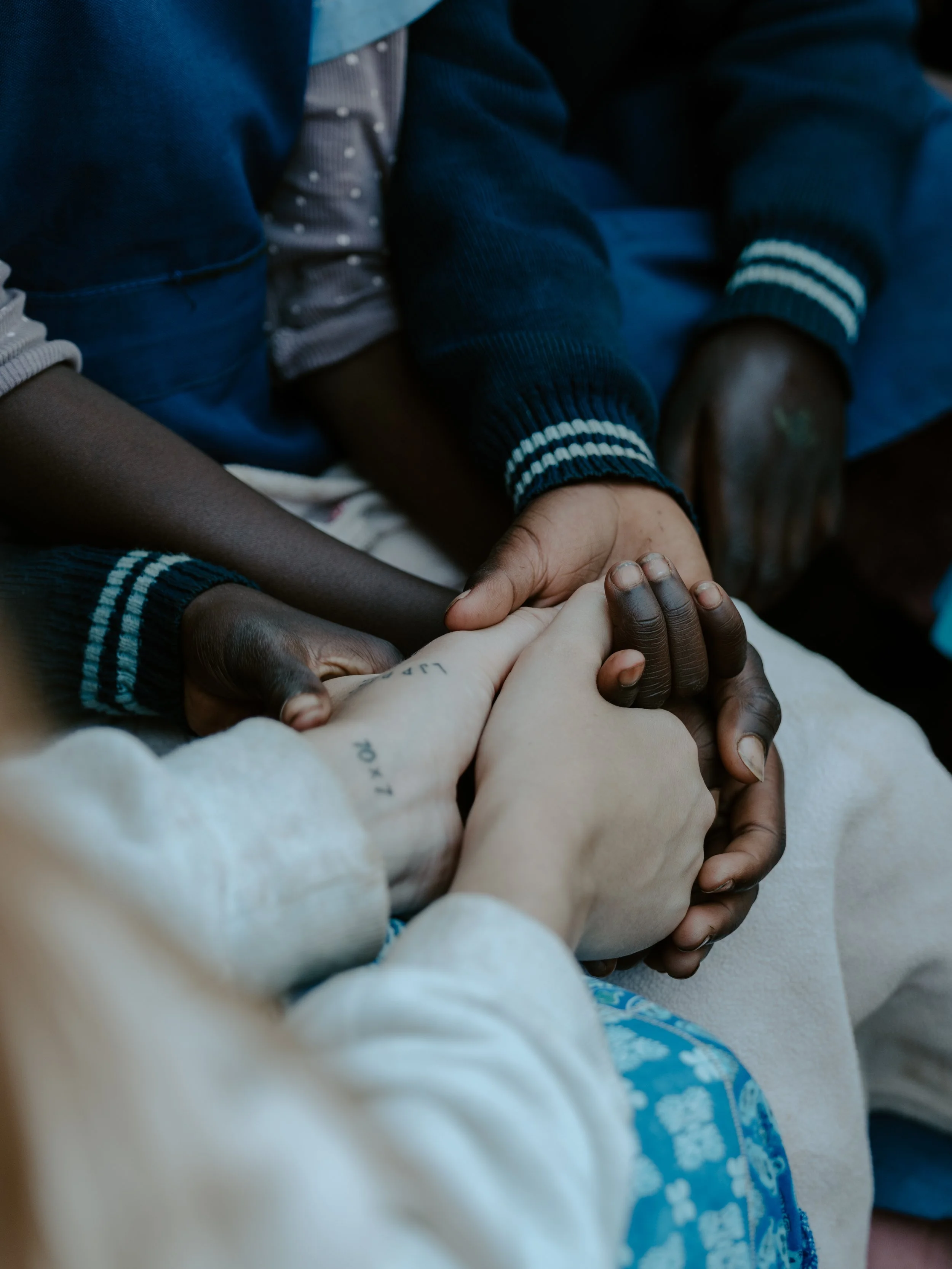 Multiple hands of children and an adult holding each other in a circle, symbolizing unity and support.
