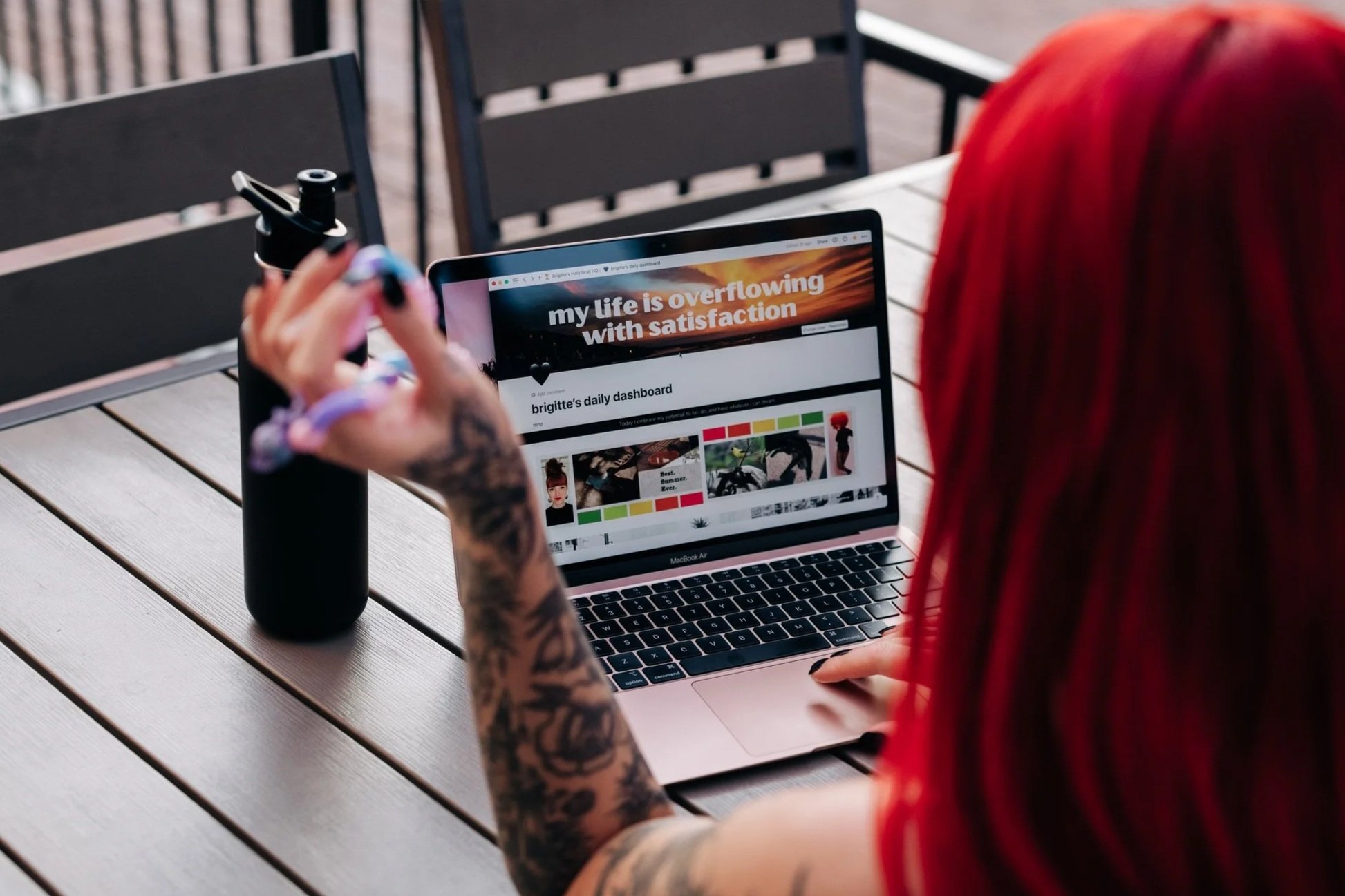 looking over brigitte's shoulder, a macbook is in focus and on the screen is a custom notion dashboard with a cover image reading "my life is overflowing with satisfaction"