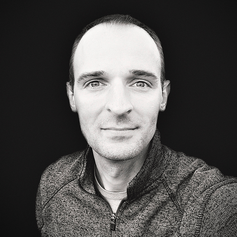 Informal black and white headshot of Luke Pieczynski wearing a dark quarter-zip