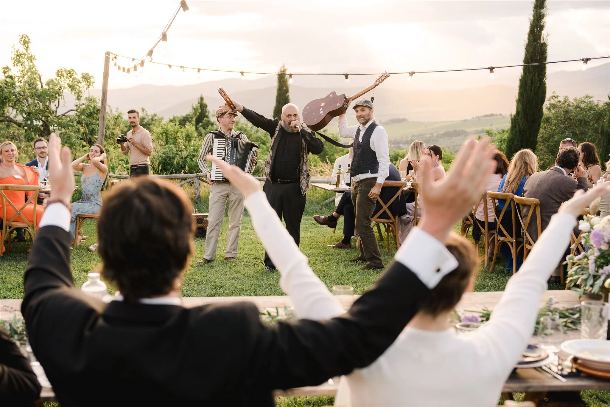 Outdoor wedding reception at Castello di Ristonchi, a wedding venue in tuscany with musicians performing and guests clapping set against a scenic landscape.