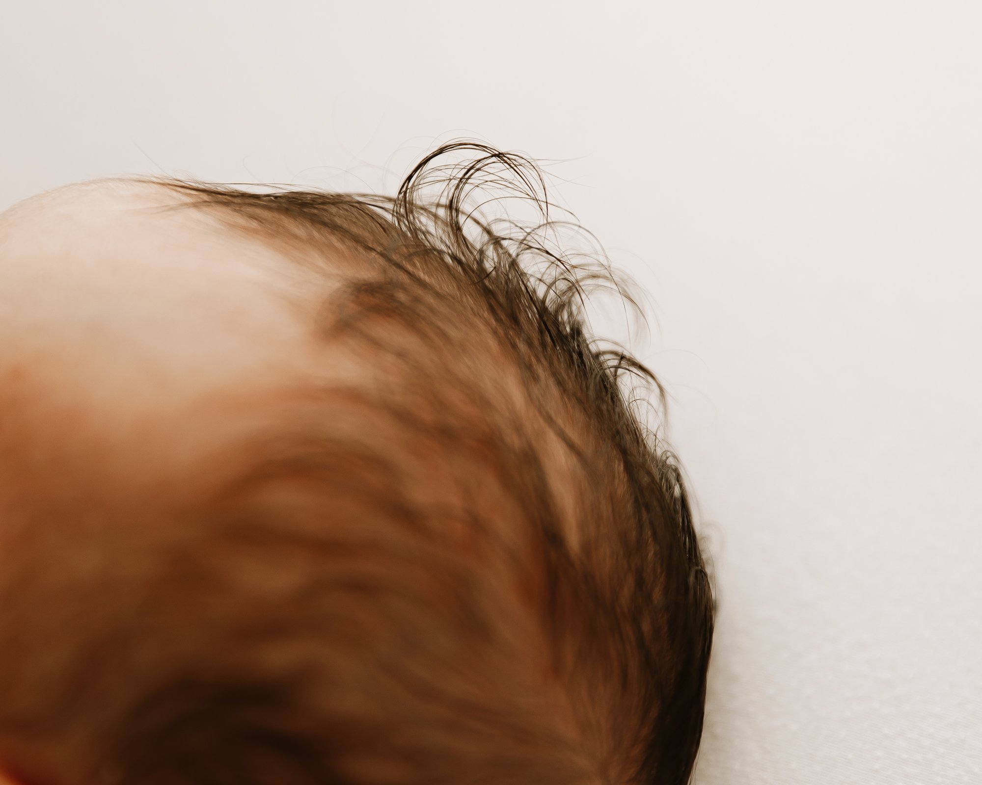 Close-up of a baby's head with brown, curly hair resting on a white surface.