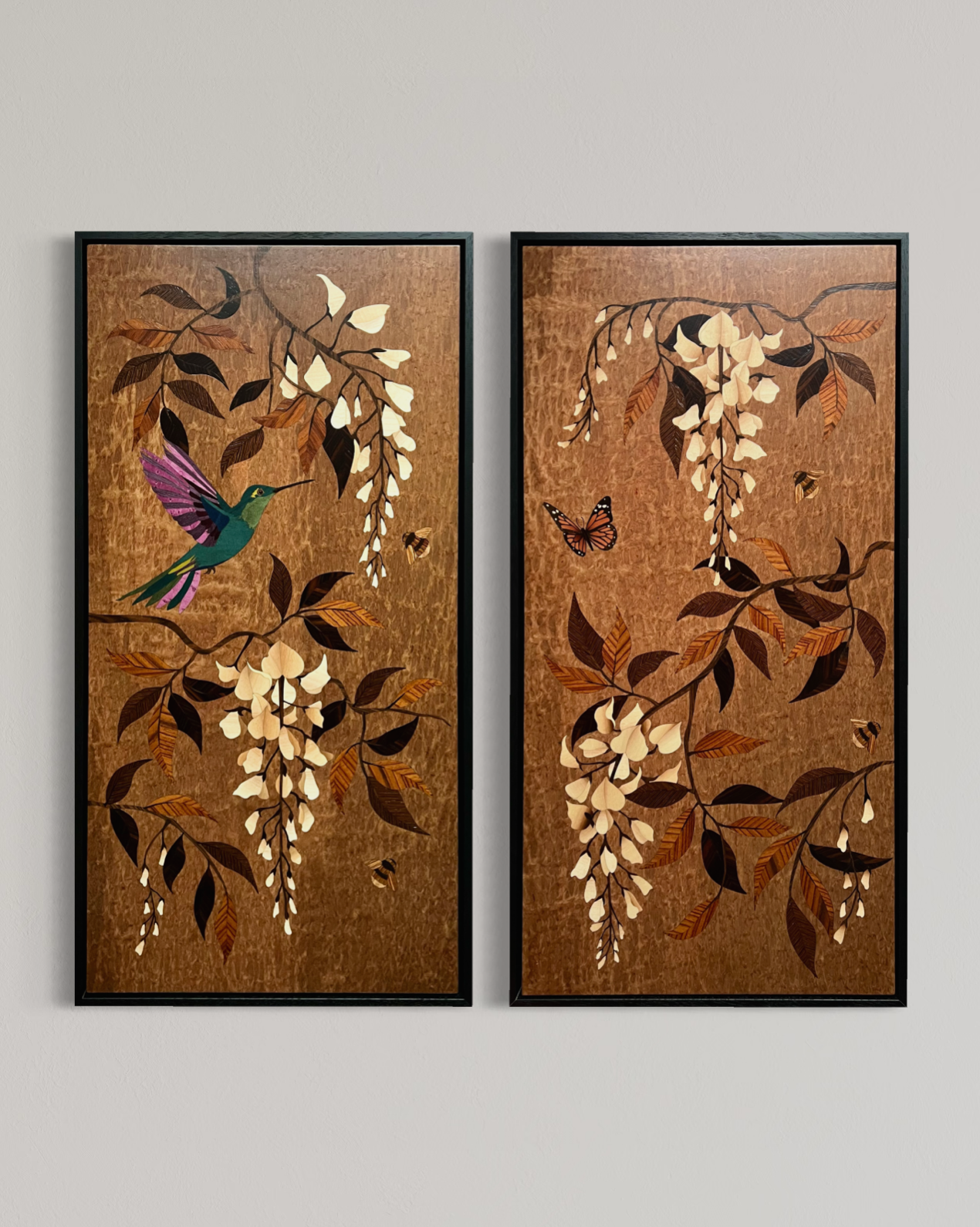 Two framed marquetry art panels depicting branches with white flowers, brown and orange leaves, a hummingbird with purple and green feathers, and orange and black butterflies, set against a brown textured background.