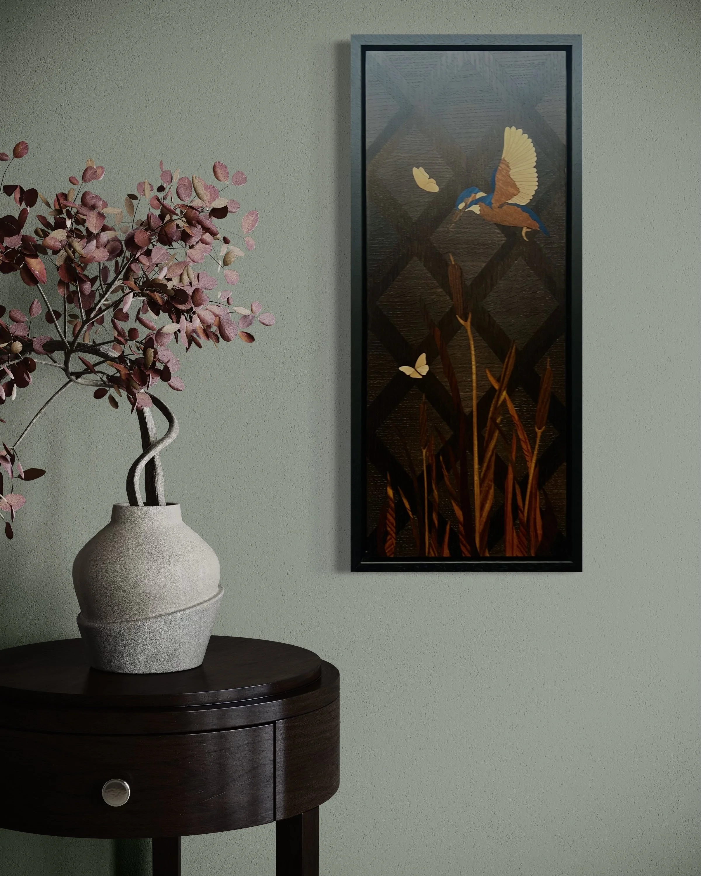Decorative marquetry wall art of a bird and butterfly on a dark background hangs on a green wall, alongside a table with a pink-leafed plant in a beige ceramic pot. Created by Carl Fox