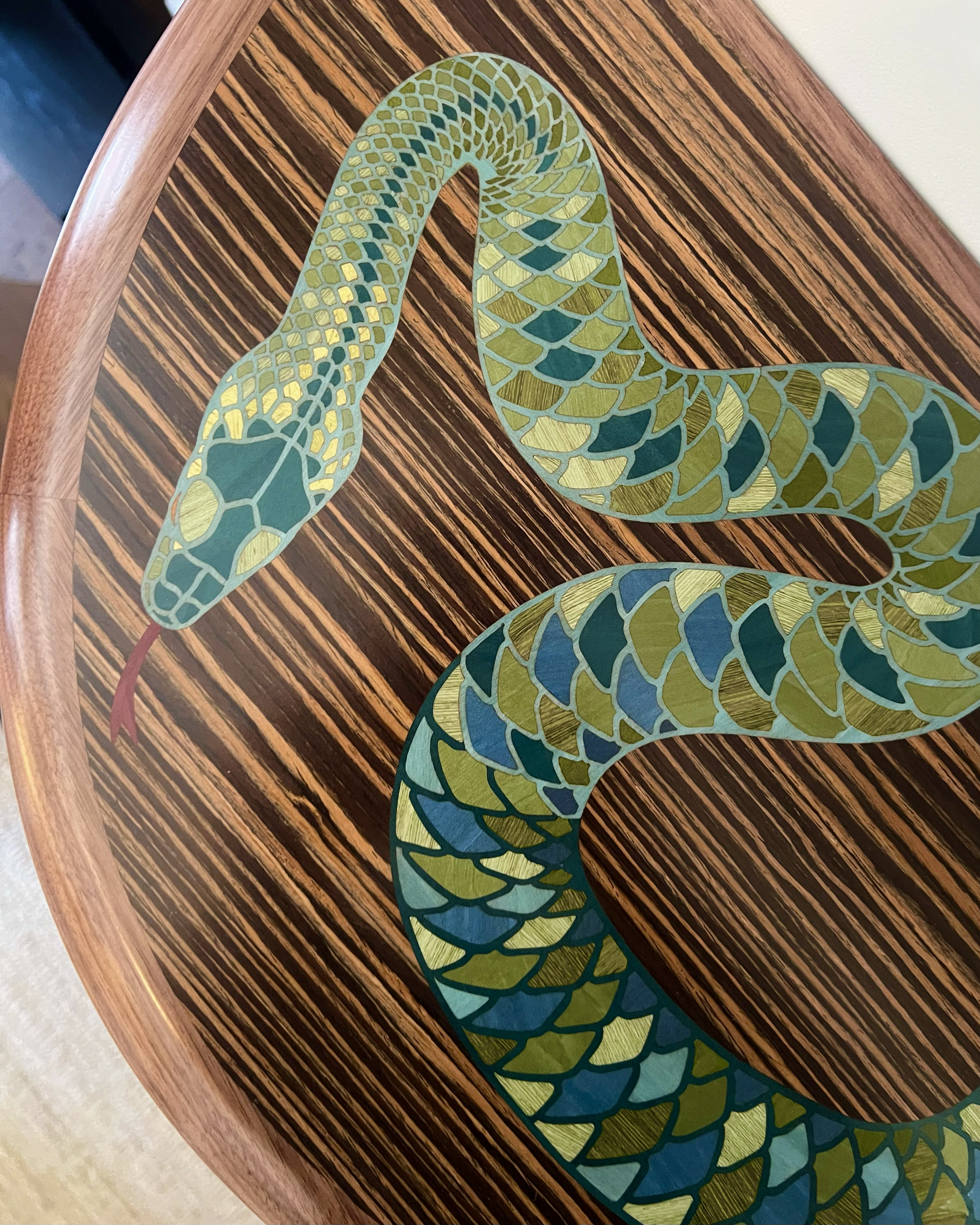 Decorative snake-shaped object with a pattern of green and blue scales, placed on a wooden table with a striped pattern.