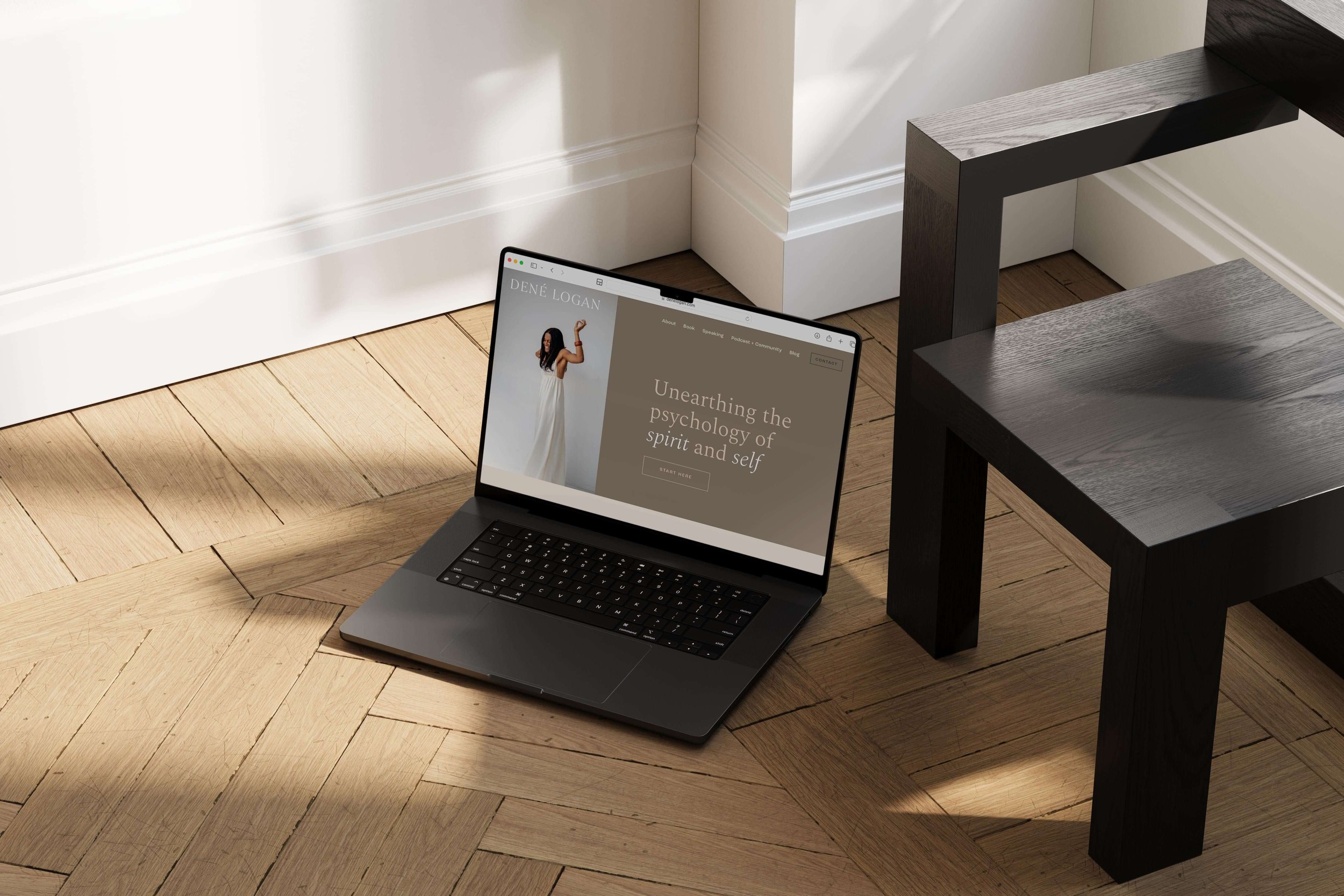 Open laptop on a wooden floor displaying a website with a woman in a white dress and the text "Unearthing the psychology of spirit and self."