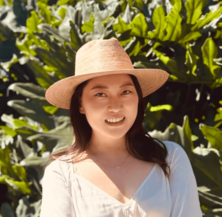 Photo of woman with dark hair and straw hat in the sun smiling