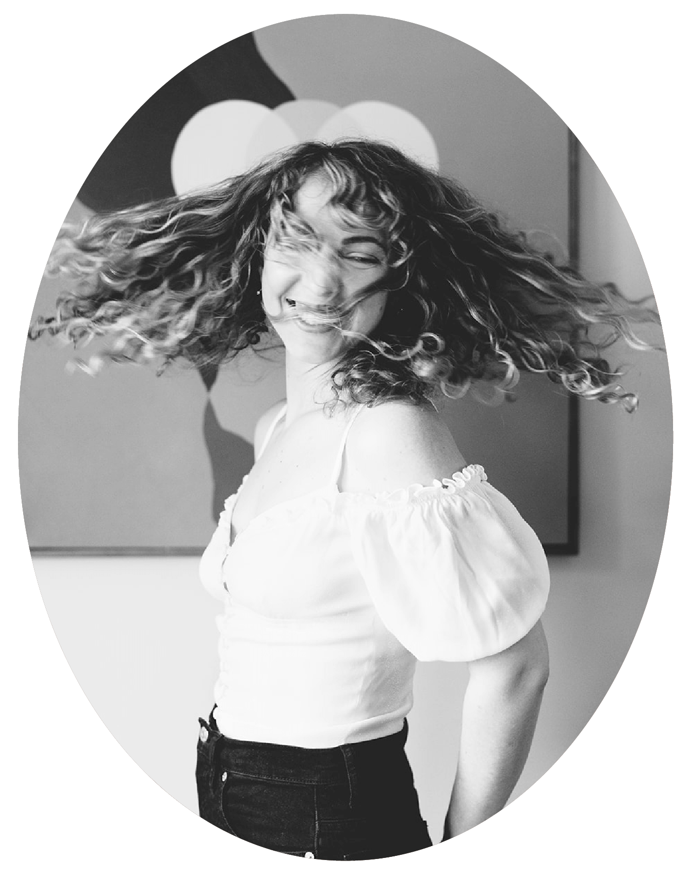 A young woman with curly hair, smiling, spinning in front of a colorful wall, captured in black and white.