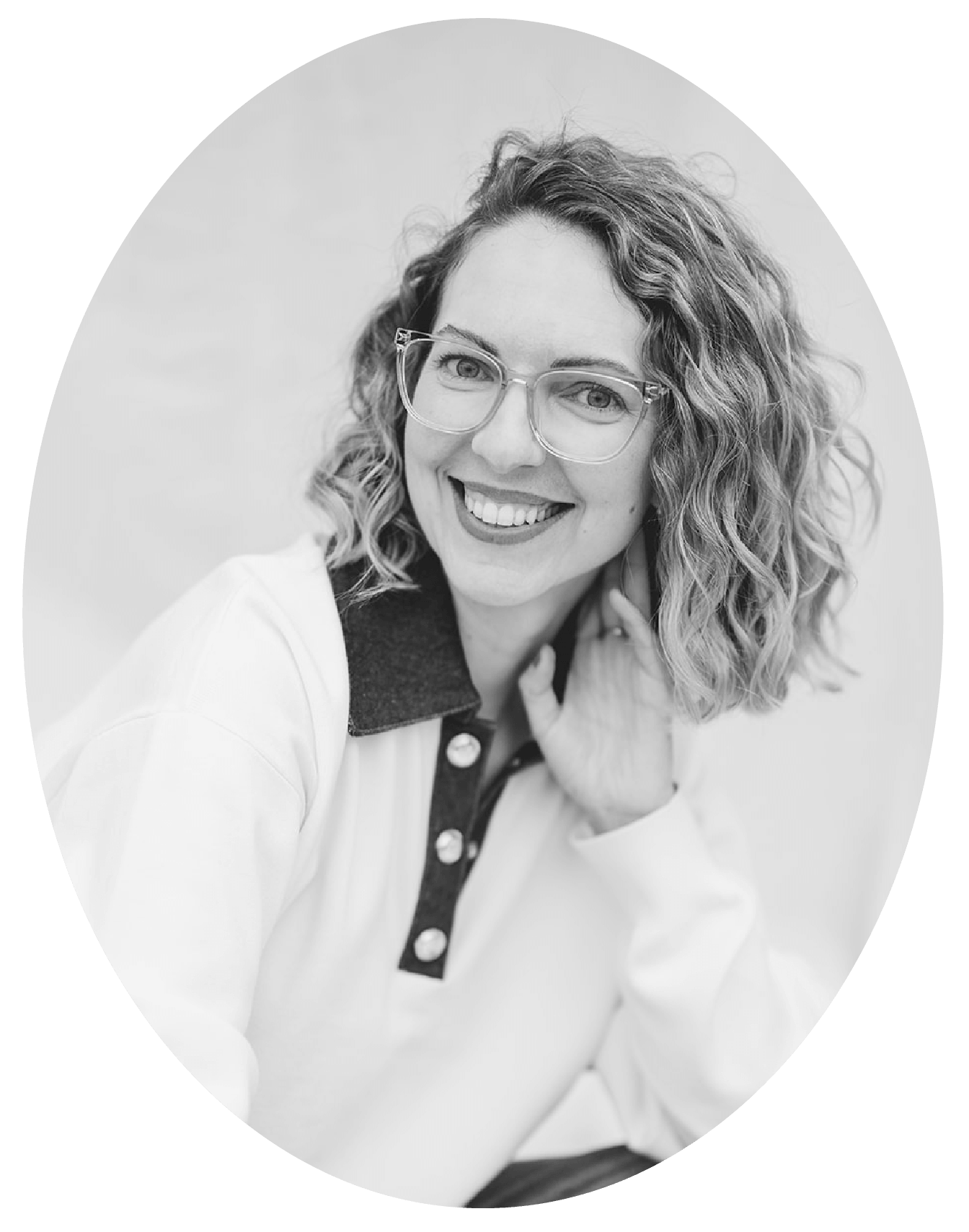 Black and white portrait of a woman with curly hair and glasses, smiling and looking at the camera, wearing a jacket with a contrasting collar and buttons.