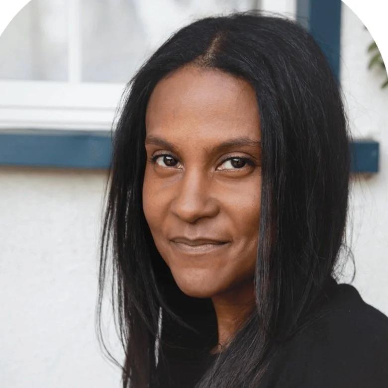 Close-up of a woman with long black hair and a subtle smile, standing outdoors near a window.
