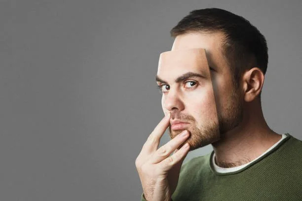 Man holding a mask of himself on his face. People lie or only show one version of themselves in Houston Therapy. Learn to be your true self with our Texas Anxiety Counselors.