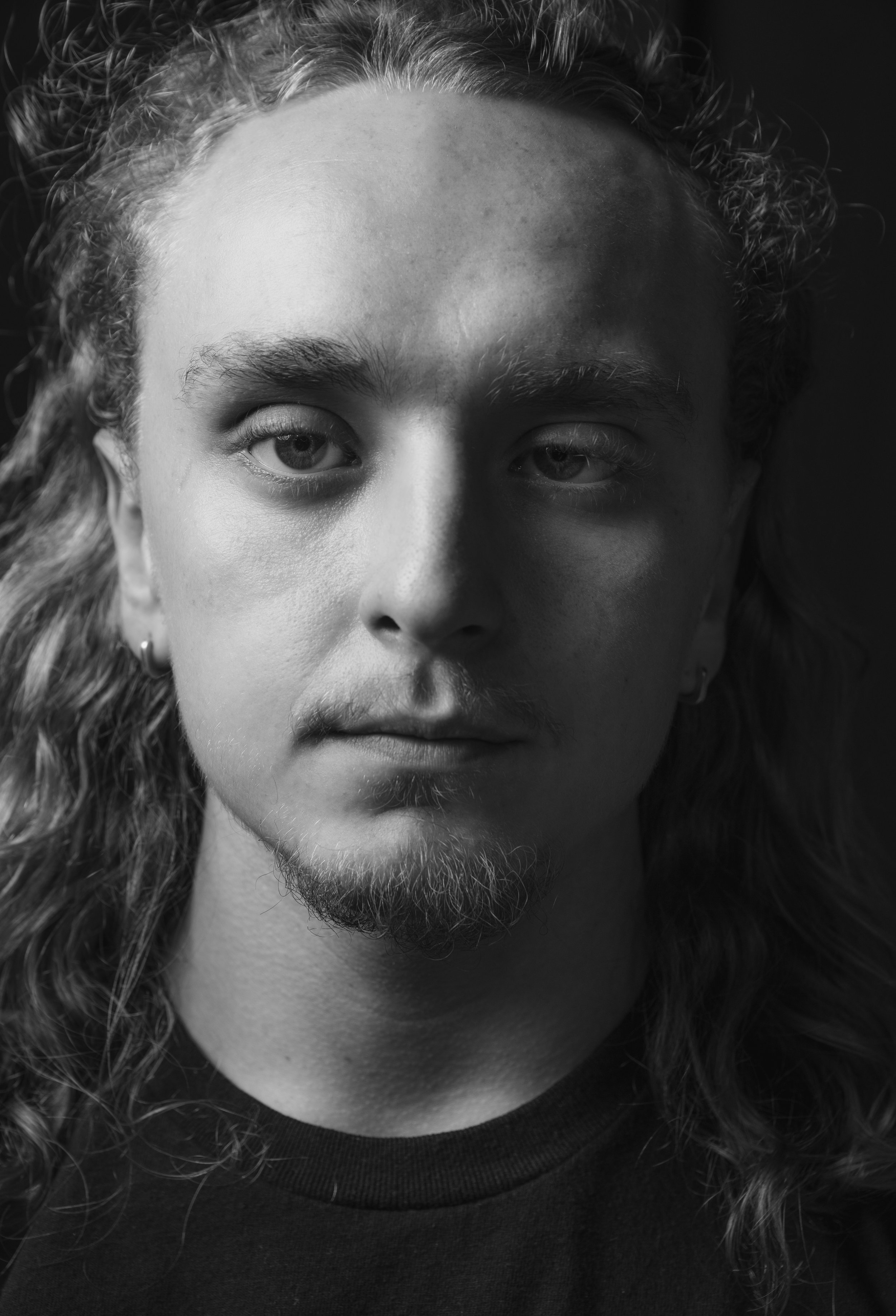 Close-up black and white portrait of a young man with long, wavy hair, a beard, and mustache.