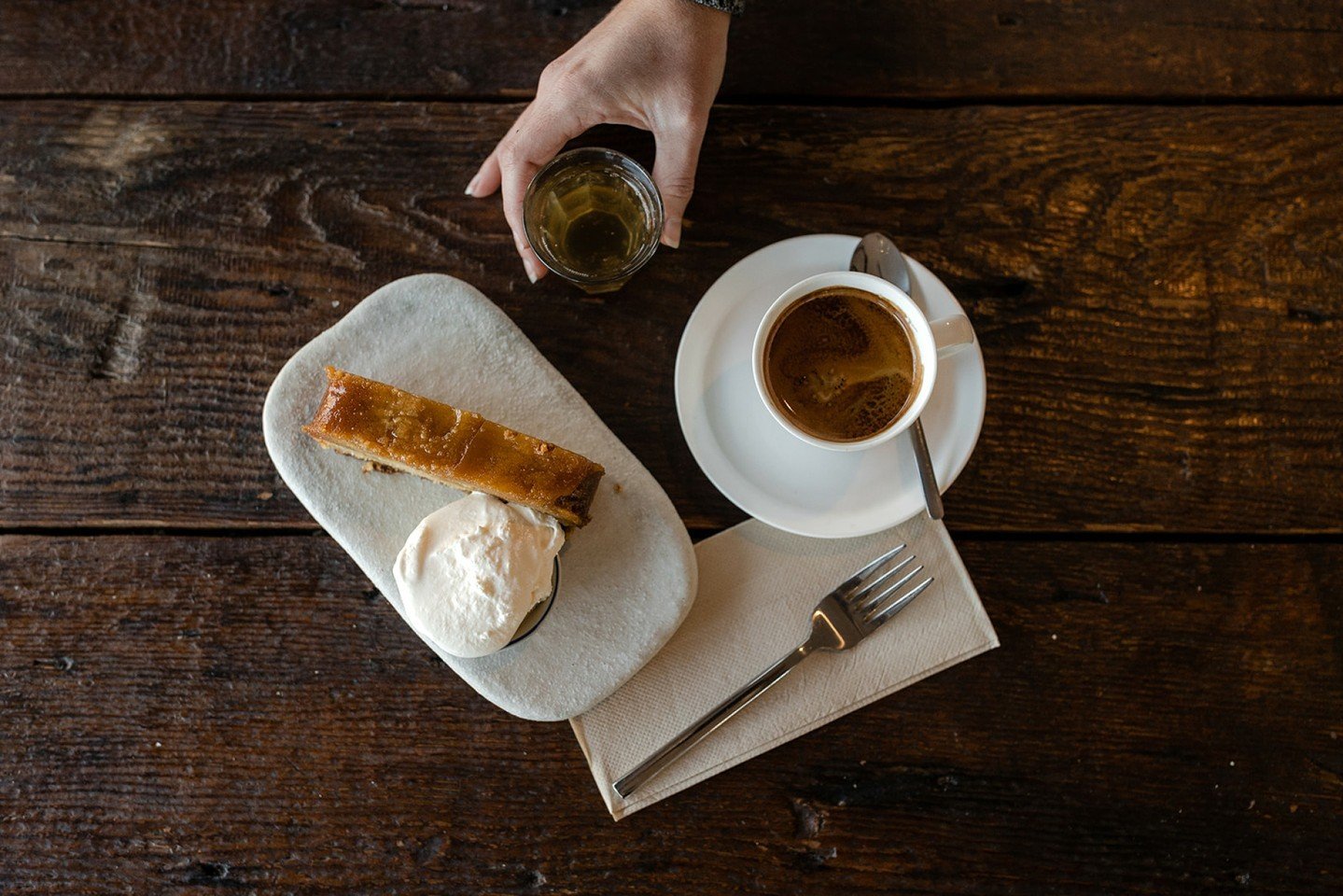 A moment just for you..

Image: an overhead shot captured on our wooden butchers block table ~ a slice of cake with a side of cream, a long black served with a little glass of cascara soda held by a staff members hand.