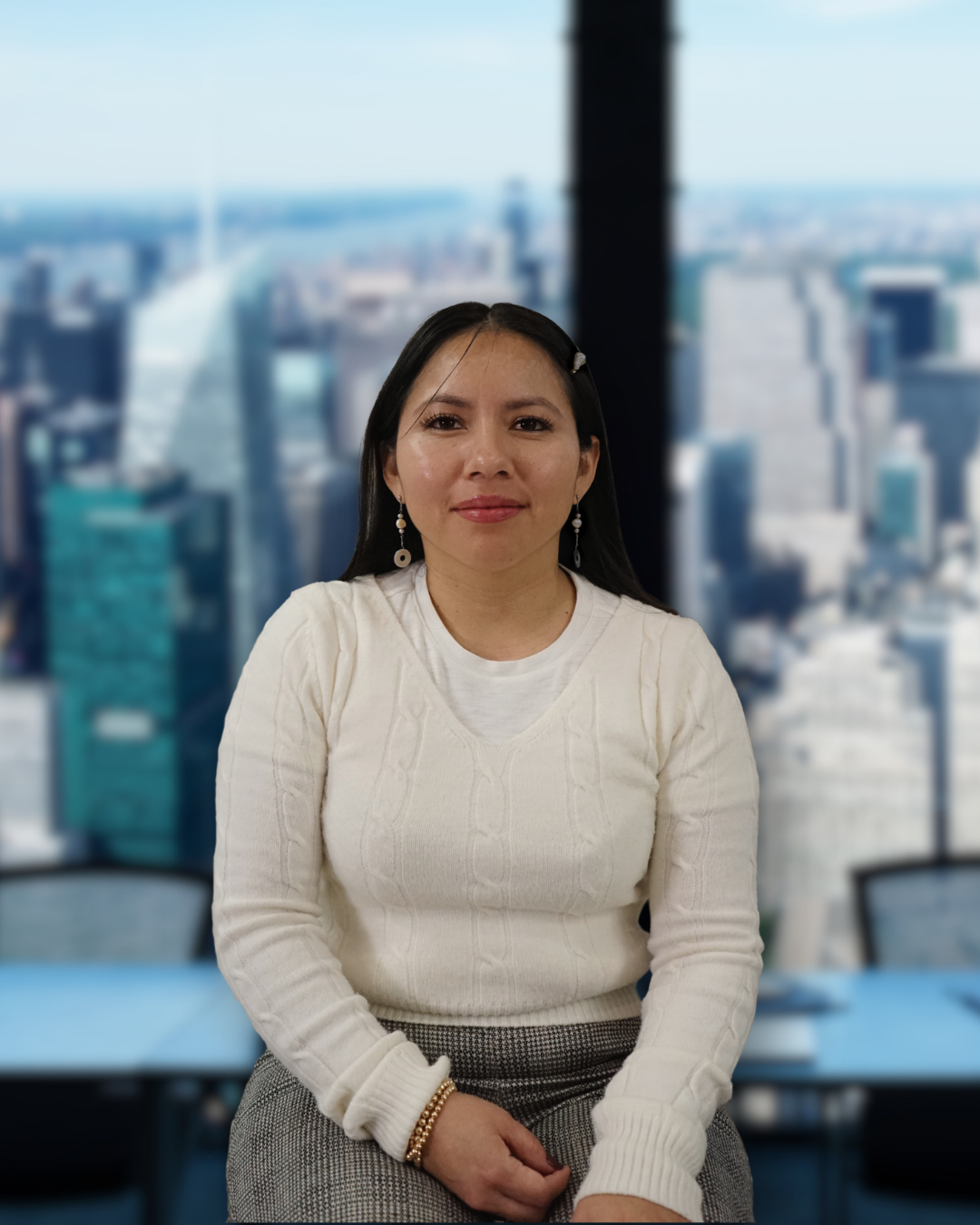 A woman sitting in front of a large window overlooking a city skyline with tall buildings.