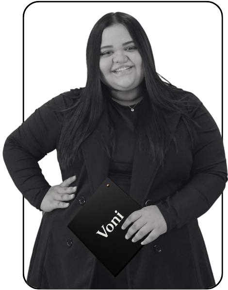 A woman with long dark hair smiling while holding a black tablet with the name 'Voni' on it, wearing a black coat against a plain background.