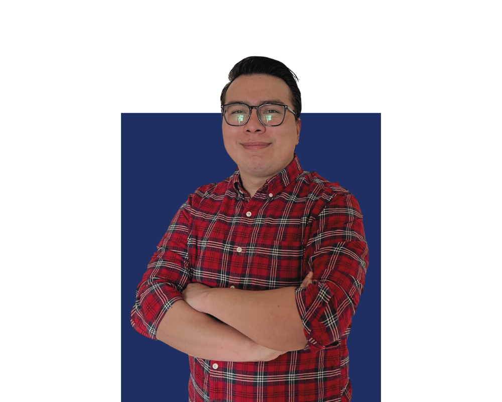 A man with black hair and glasses wearing a red plaid shirt, standing with arms crossed against a background with dark blue and purple sections.