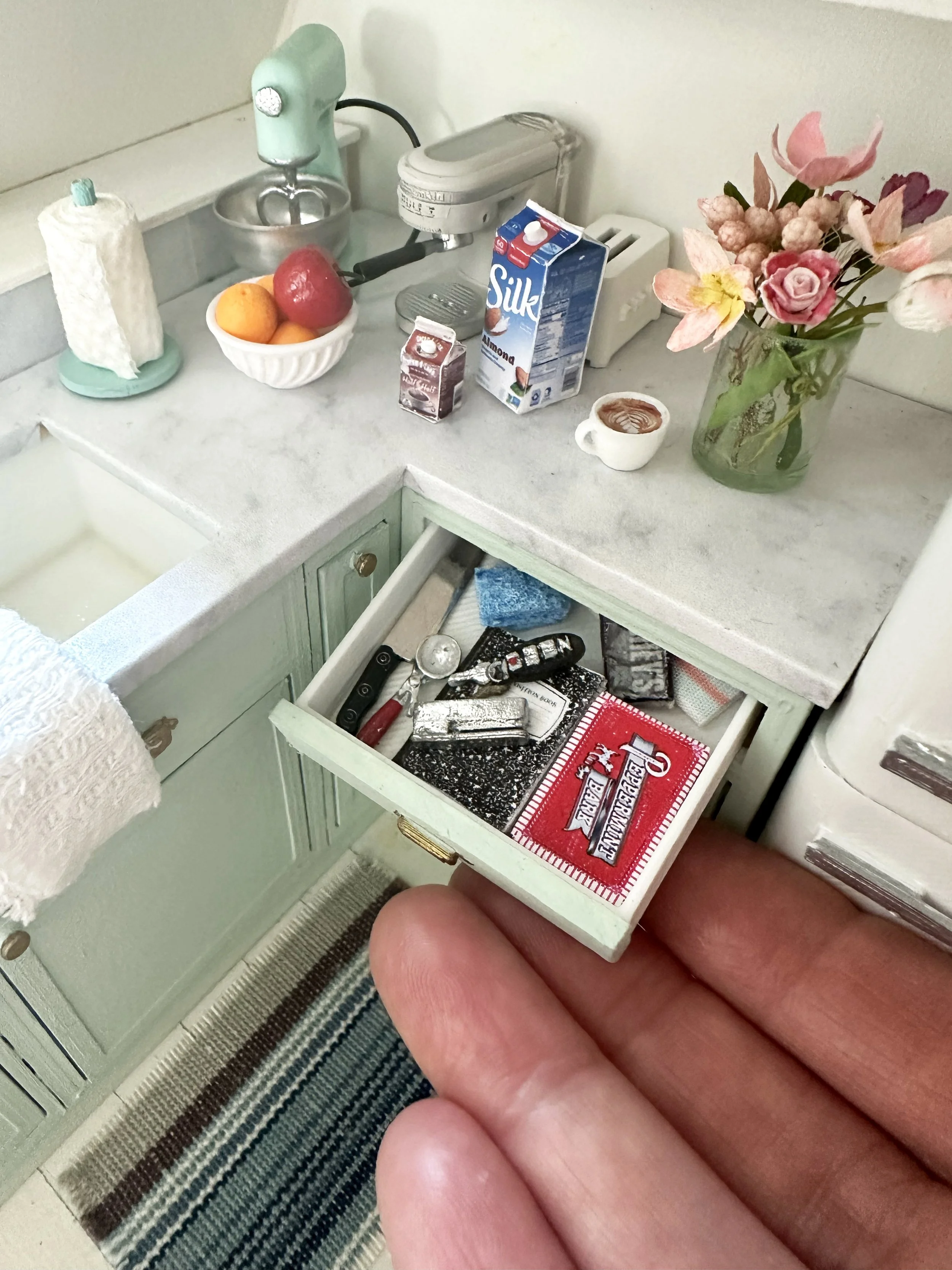 A person's fingers holding open a small drawer with a box of Red Bird cigarette matches inside, resting on a striped rug near a green cabinet.