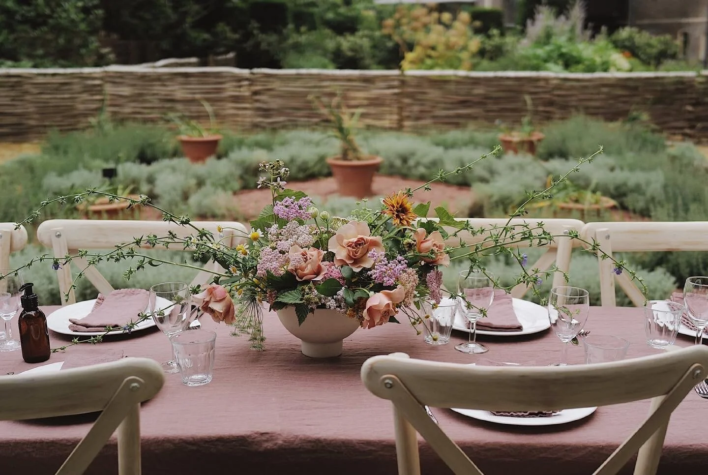 Outdoor table setting with floral centerpiece and rustic garden backdrop.