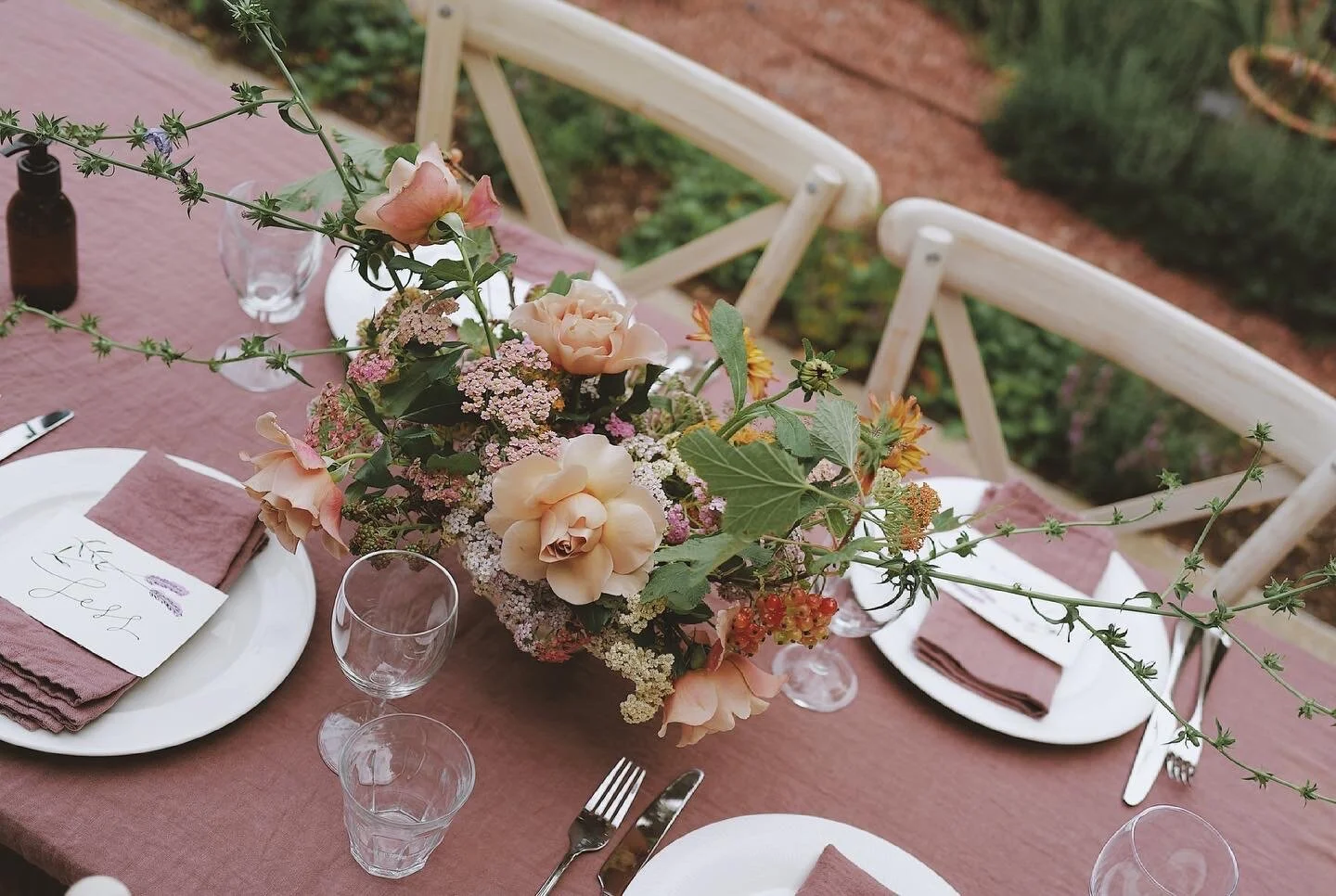 Elegant outdoor table setting with floral centerpiece and pink tablecloth.