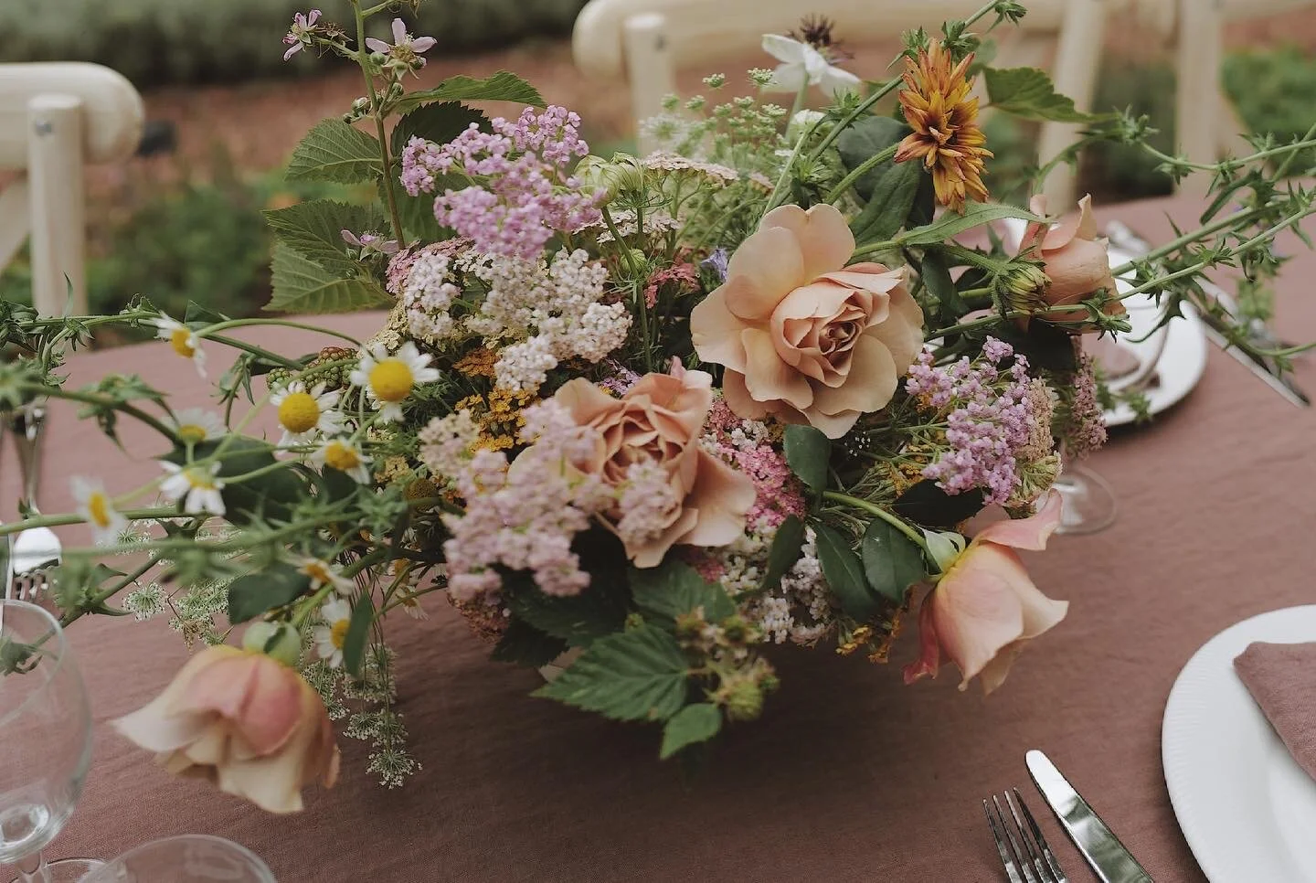 Floral centerpiece on a dining table with roses, daisies, and mixed flowers