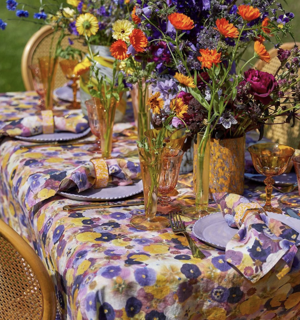 Floral-themed table setting with colorful flowers, patterned tablecloth, glassware, plates, and napkins.