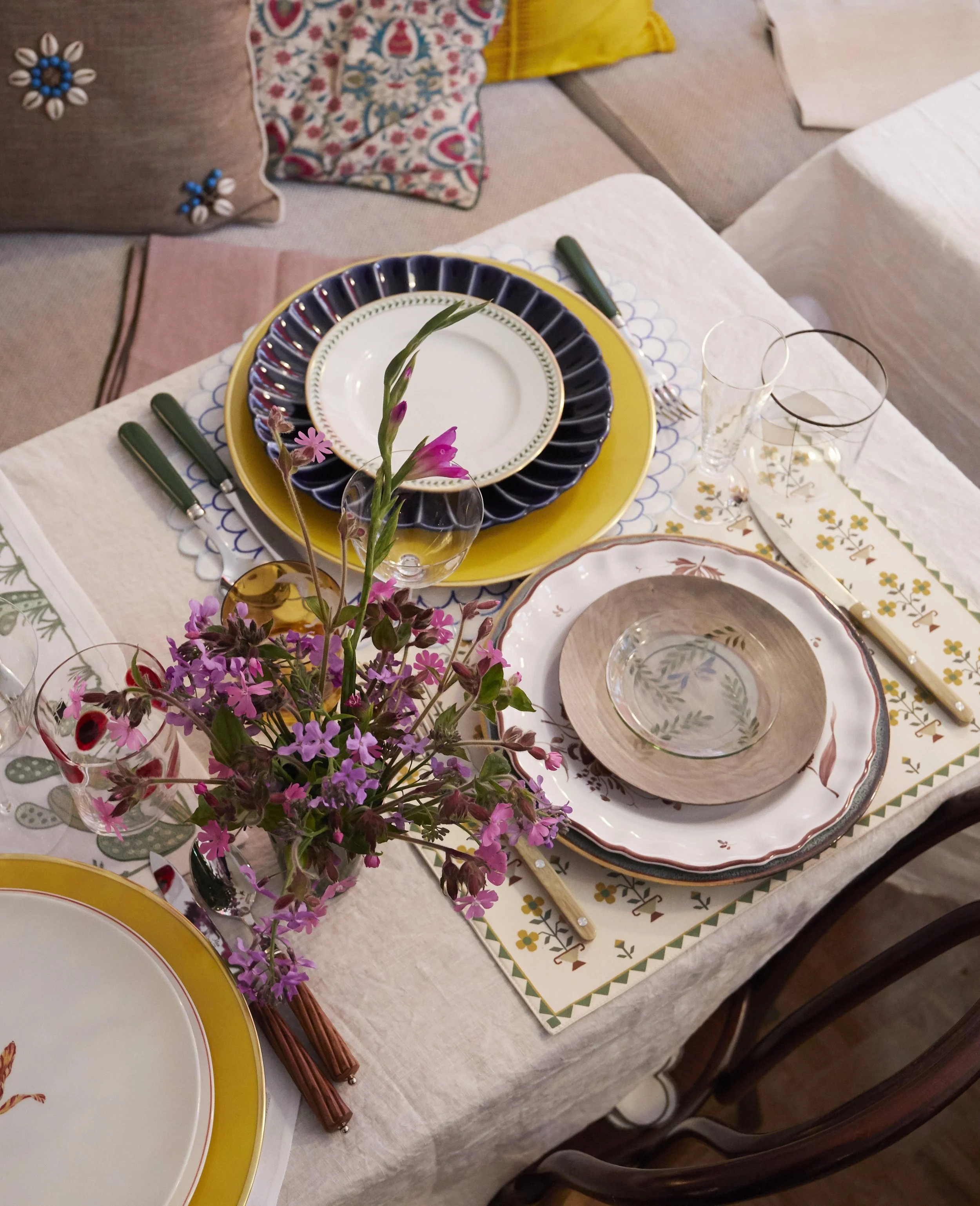 Elegant table setting with layered plates, floral centerpiece, glassware, and cutlery on patterned tablecloth.