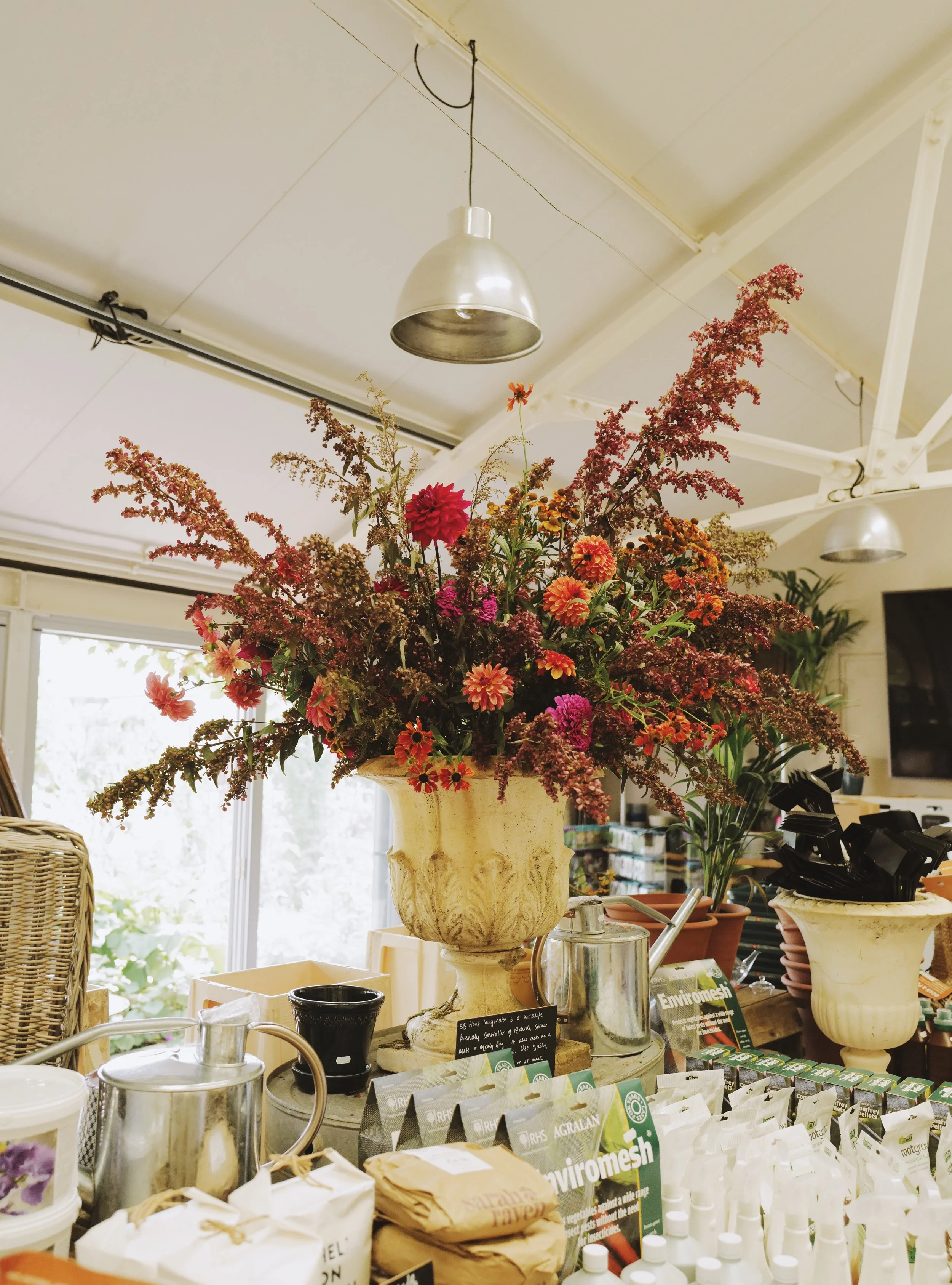 Florist shop interior with large floral arrangement in vase, garden tools, and products on display.