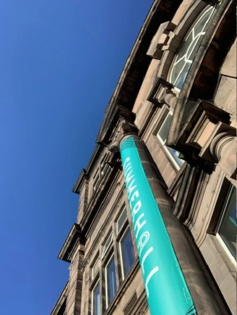 ID: A low angled photo taken looking up at the Summerhall banner and building façade.